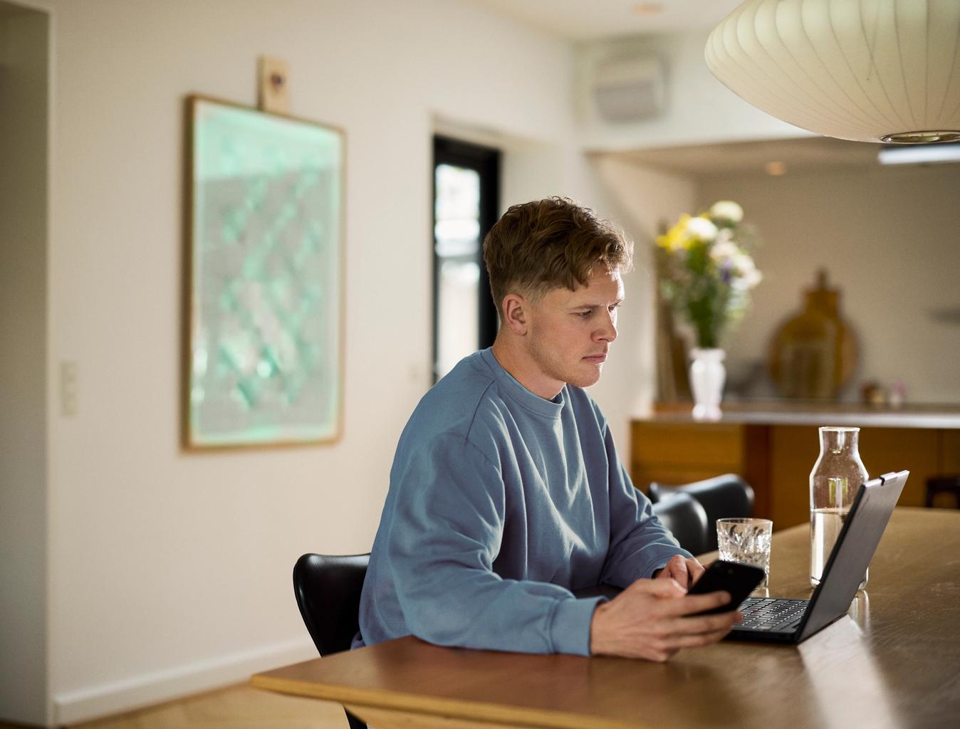 Mand sidder på spisebord med hans computer og telefon og tjekker noget