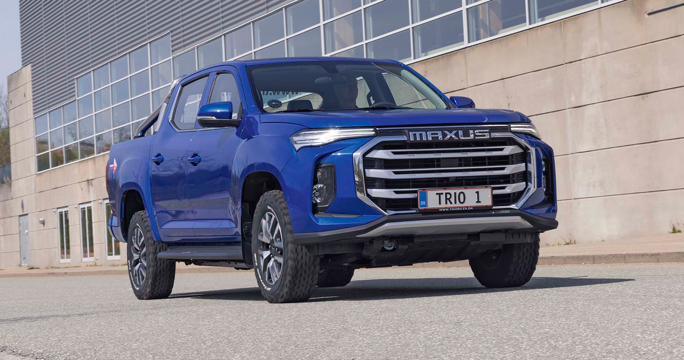 En blå Maxus eT90 holder parkeret foran en mur