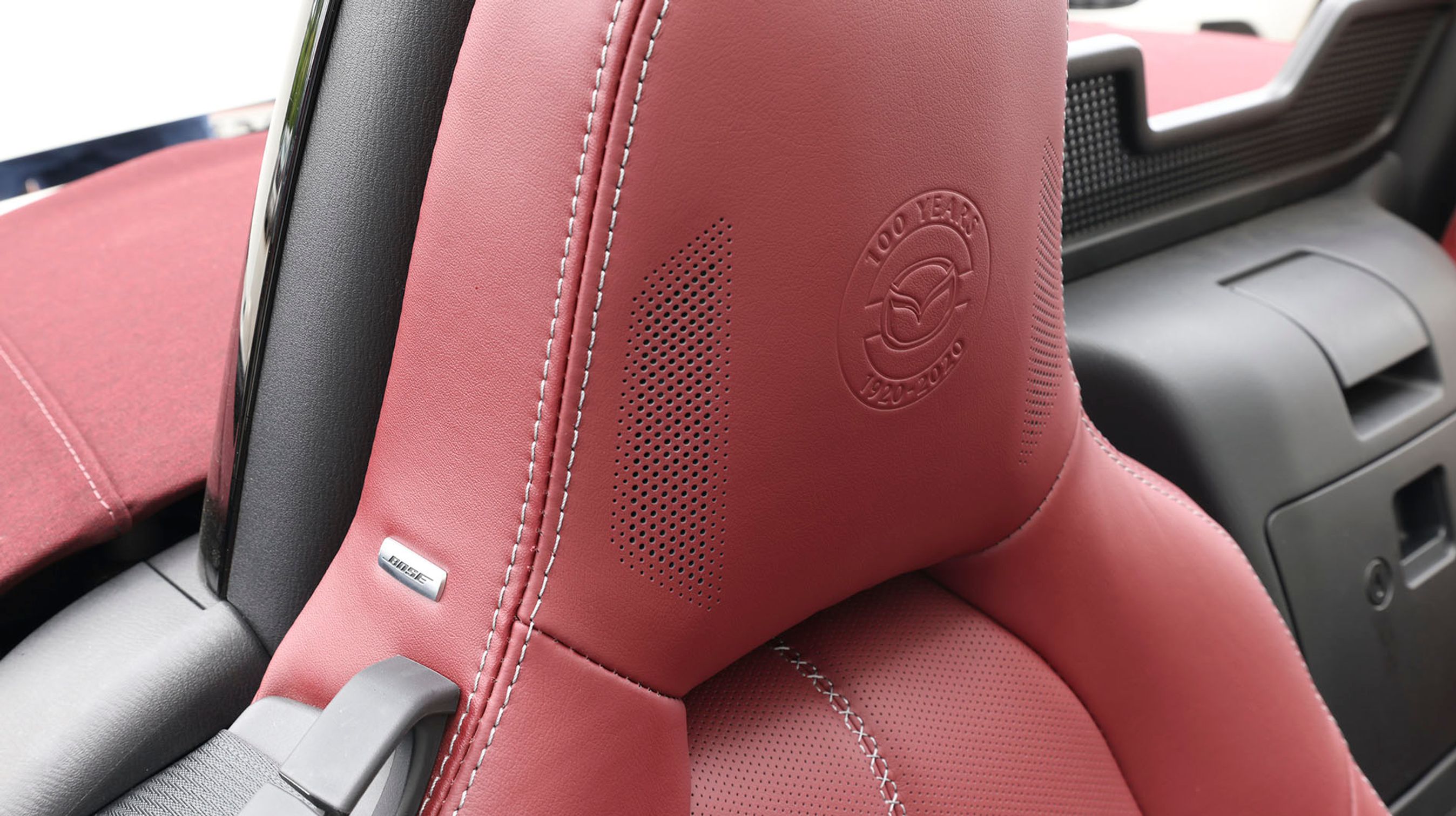 Der er 100-årsjubilæumslogo præget ind i de røde lædersæder. Men mere glad bliver du for de små Bose-højttalere, der også er indbygget i sædet. Det giver lyd der, hvor hovedet er. Godt tænkt.