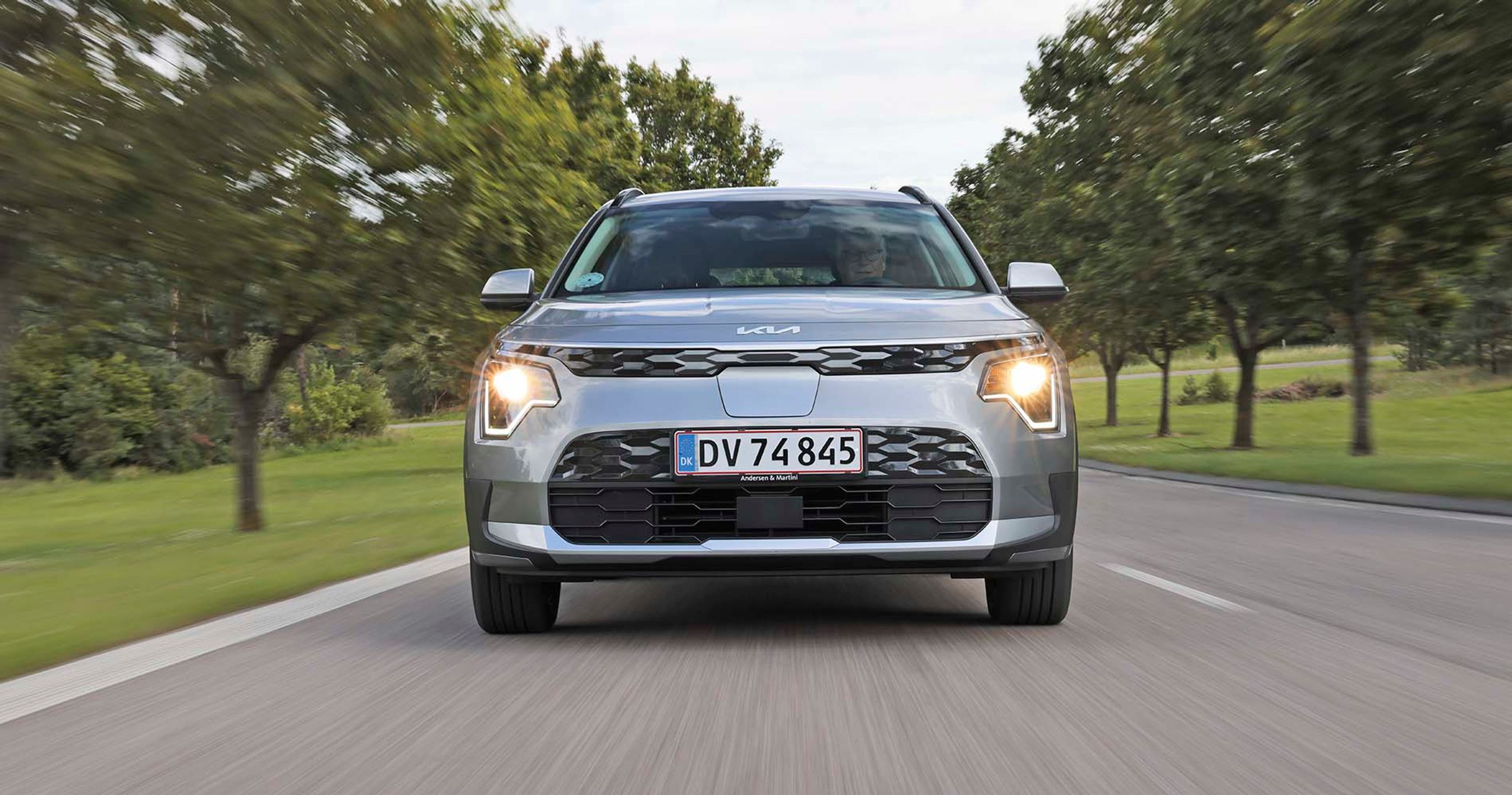 Elbilen Kia Niro EV set forfra, mens den kører på en allé.