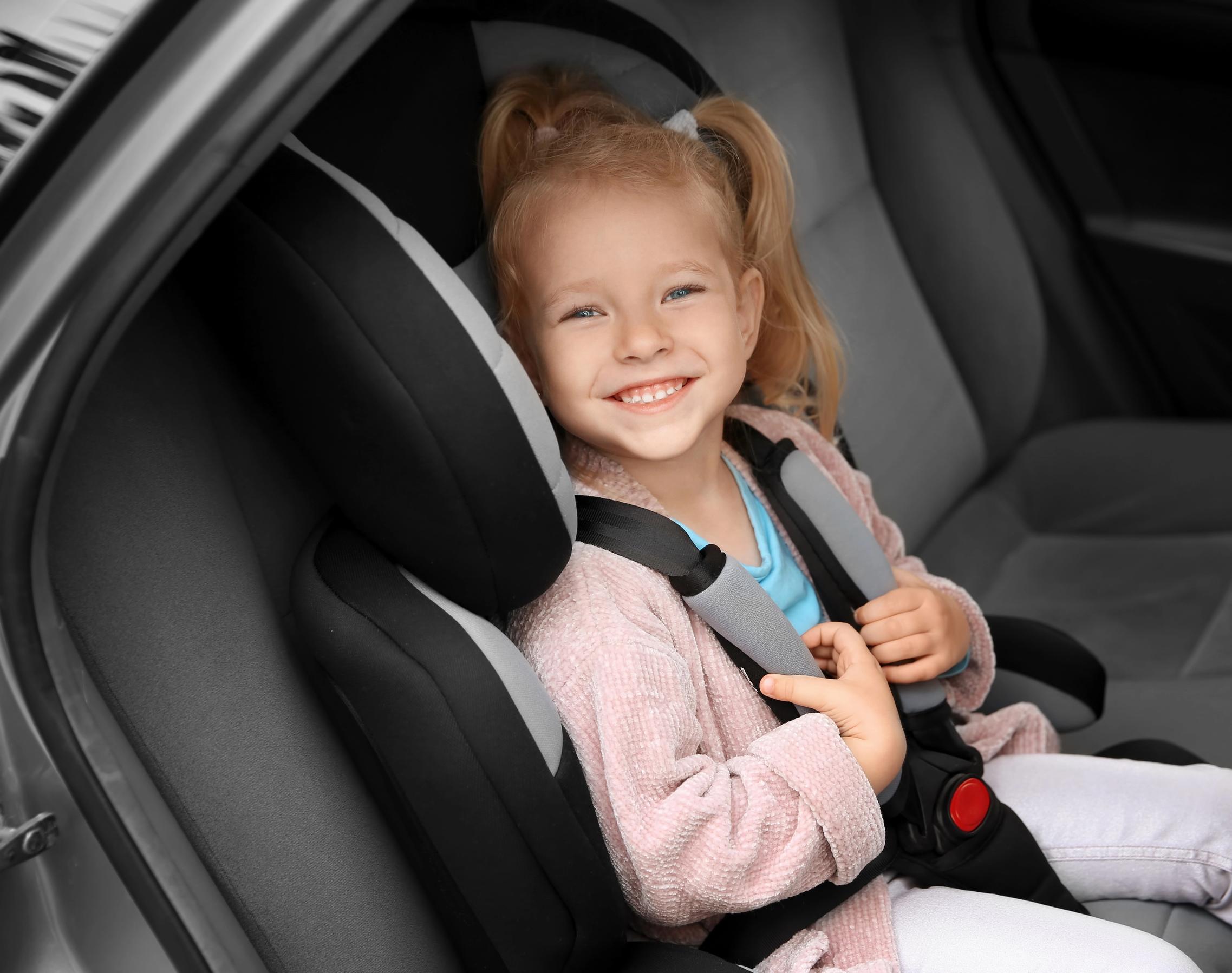 Piger sidder i autostol på bagsædet af en bil og smiler.