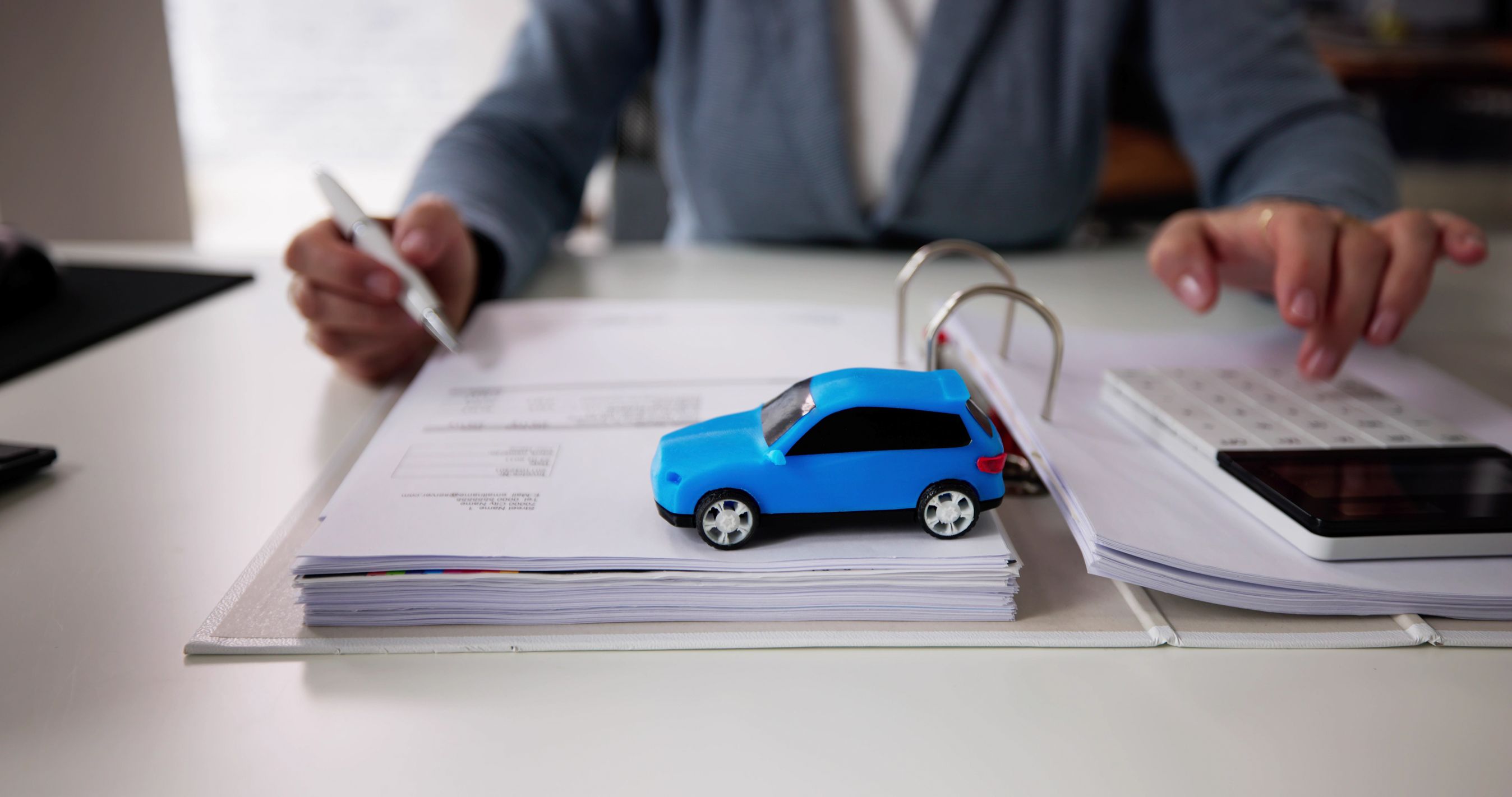 Mand bladrer i papirer i ringbind, og ovenpå er placeret en blå legetøjsbil.