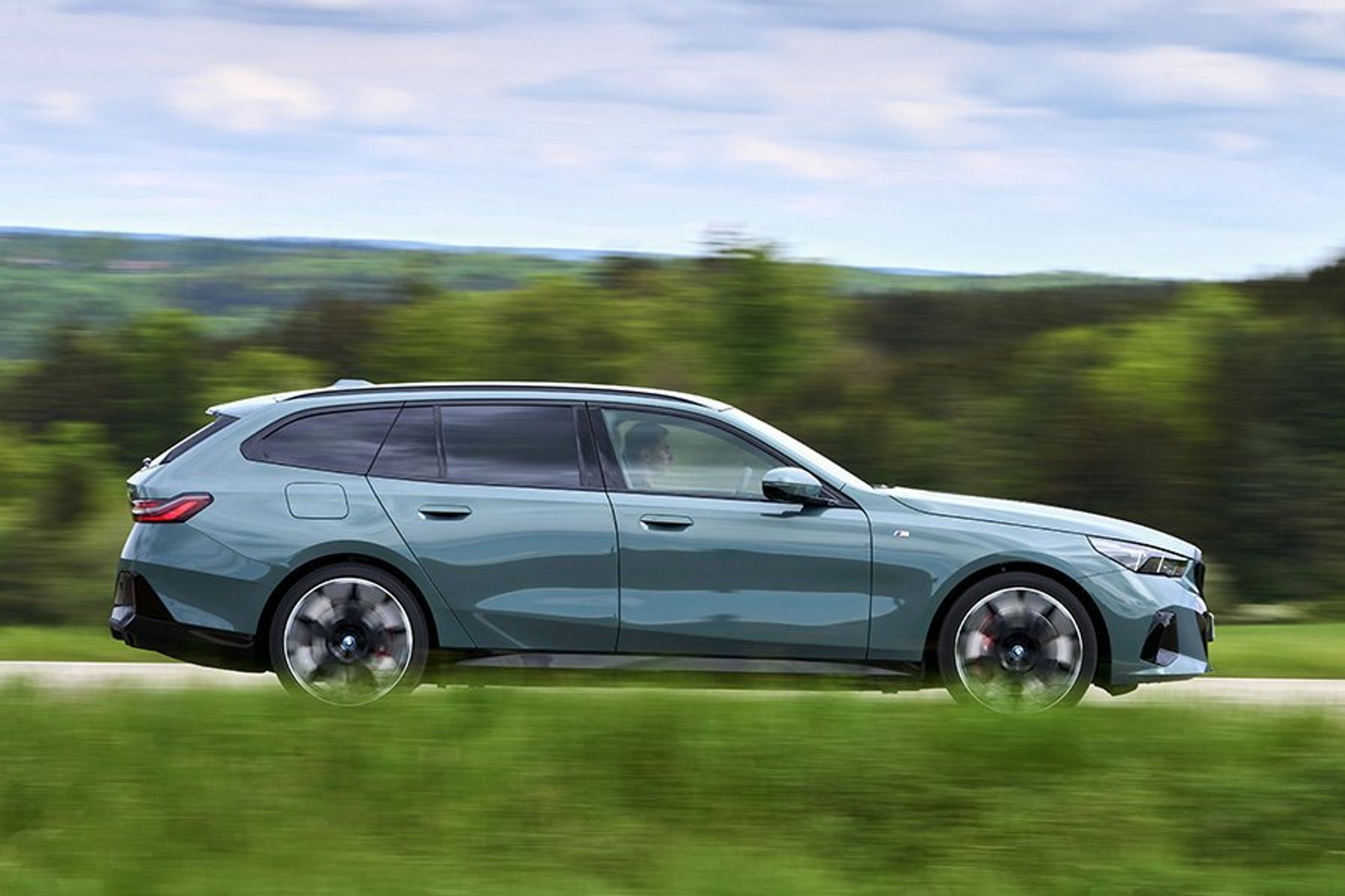 BMW i5 Touring set fra siden, mens den kører gennem et grønt landskab