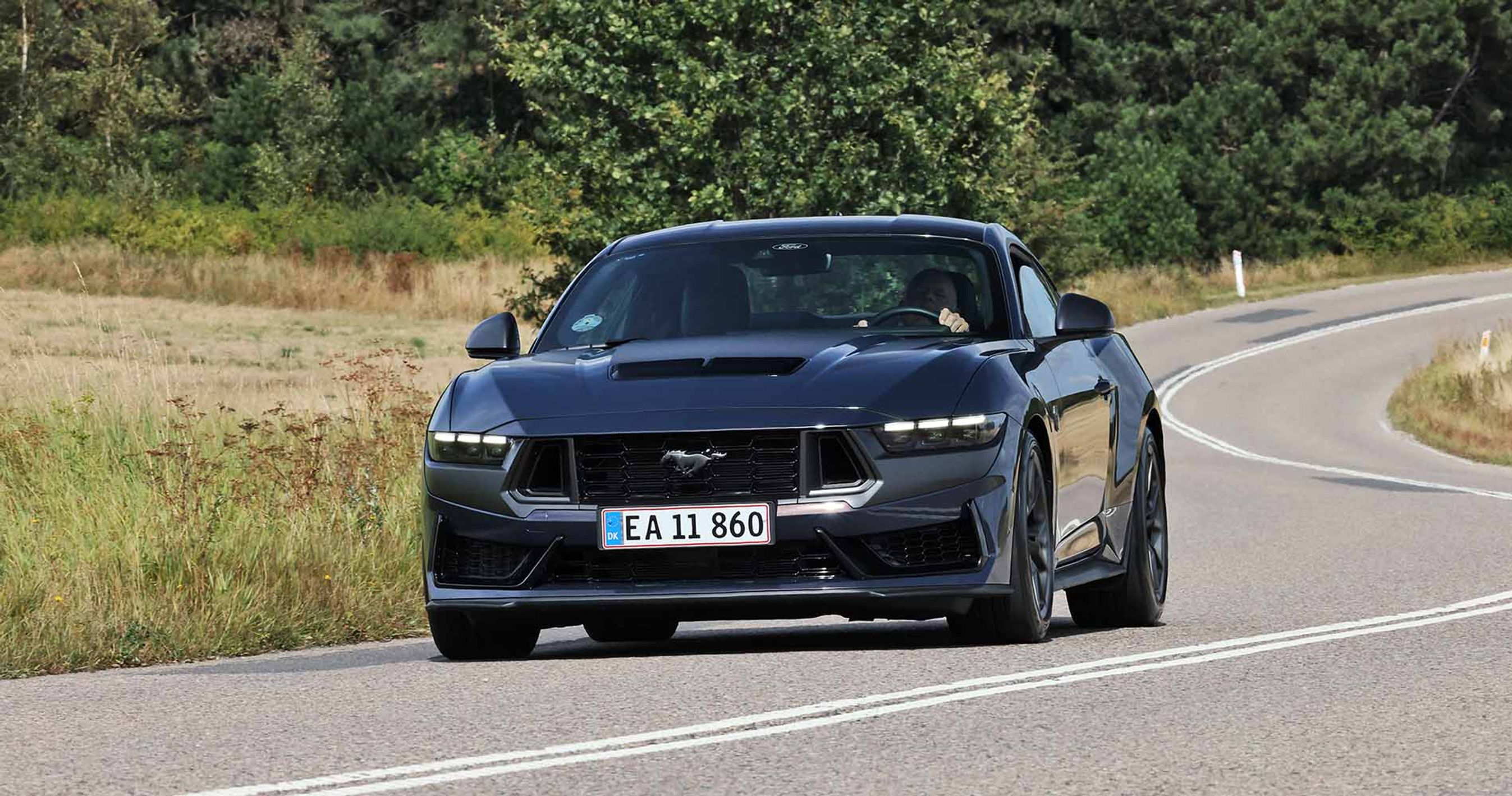 En sort Ford Mustang set forfra, kørende gennem en naturskøn rute.