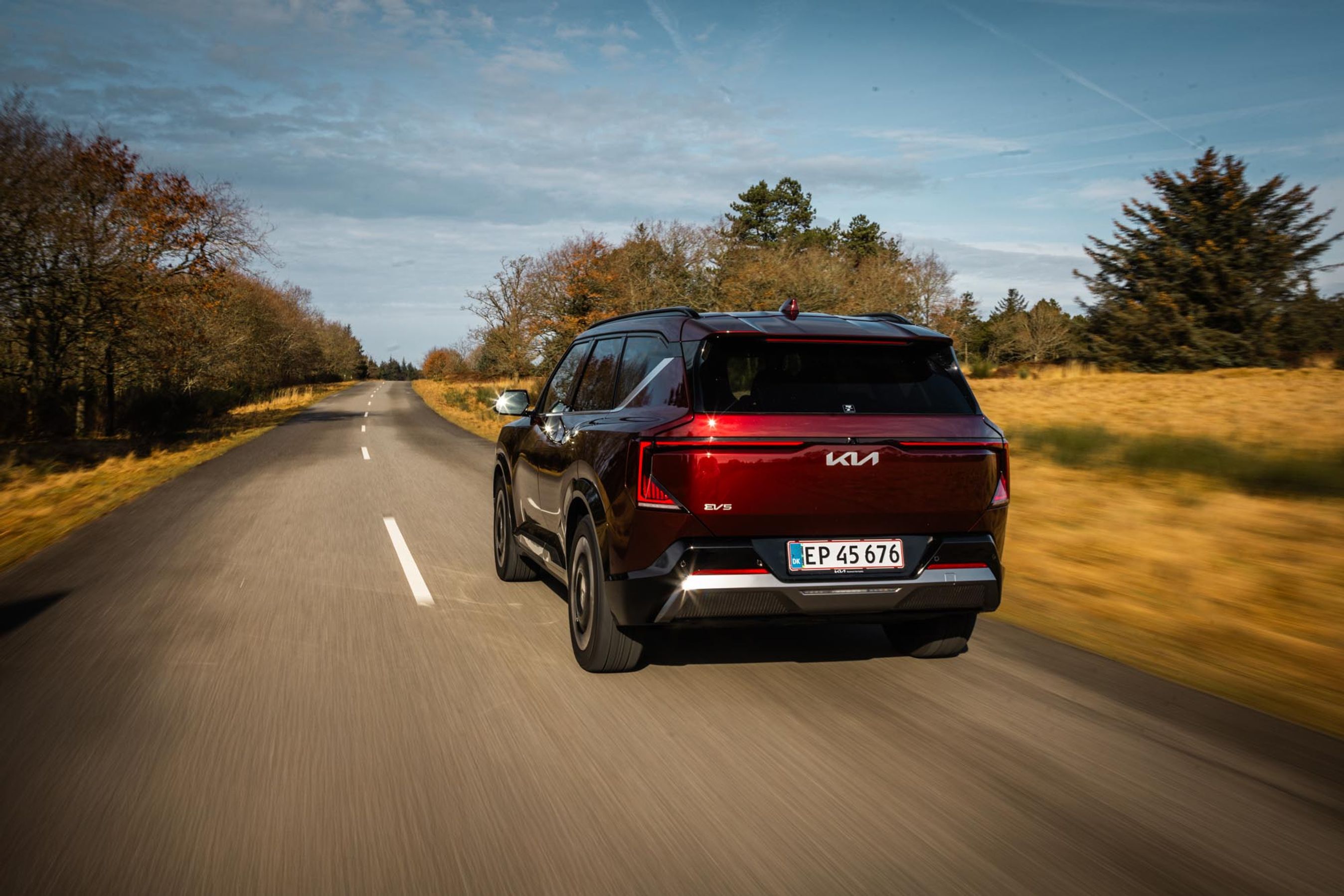 En mørkerød Kia EV5 kører på en landevej.