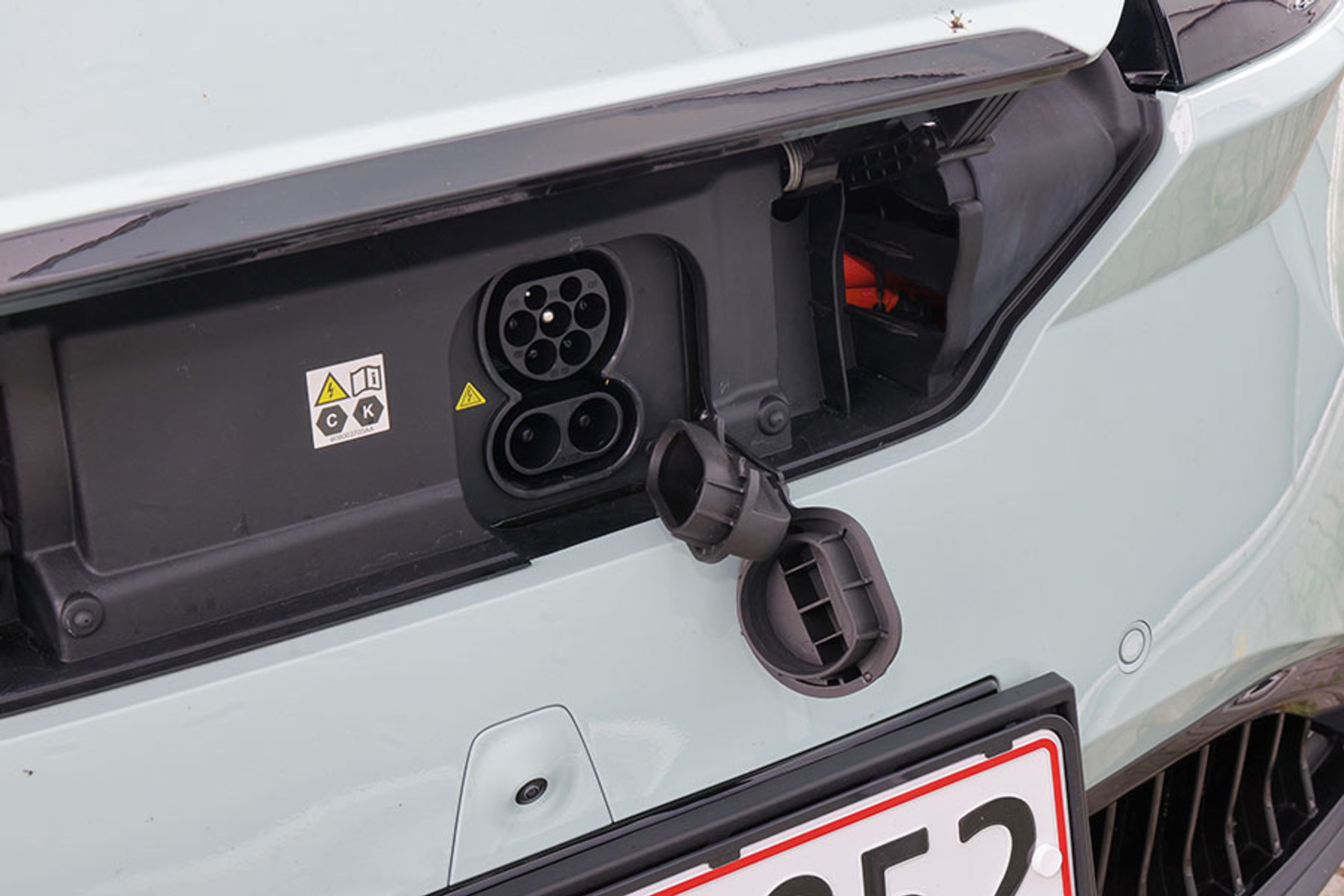 Få biler har ladestik foran, men selvom det kan være smart i forhold til hjemmeladning, så er adgangen i Omoda lidt besværlig. Låget foran stikket udløses på en knap i kabinen, og der er plastpropper hen over begge ladestik. Det er mere besværligt end i de fleste konkurrenter. 