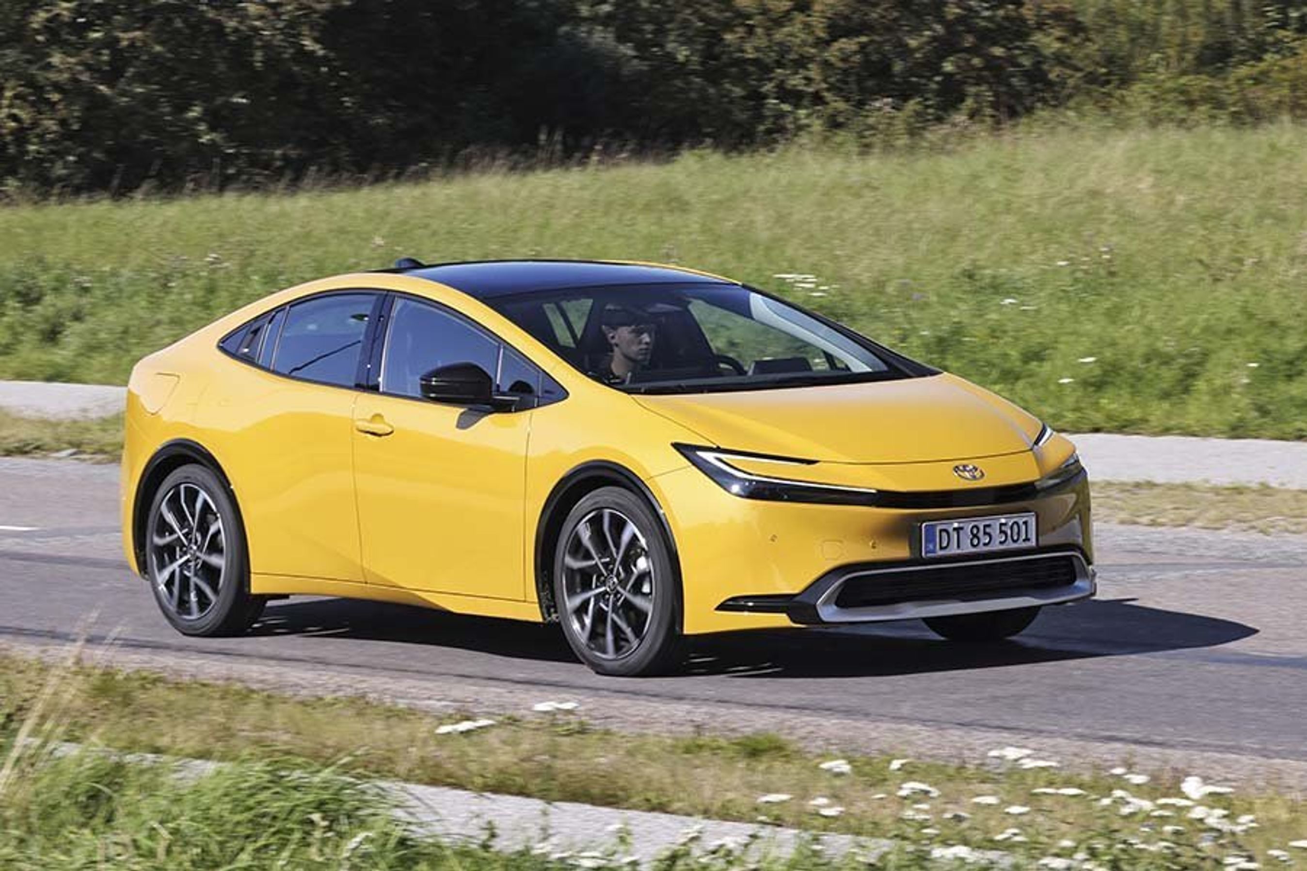 En gyl Toyota Prius kører på en landevej.