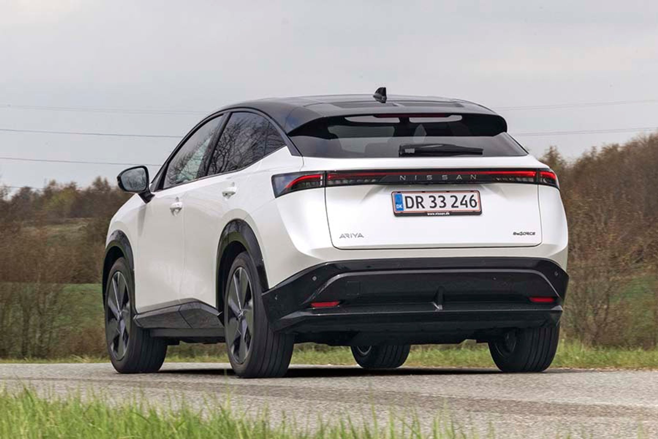 En hvid Nissan Ariya elbil set bagfra, mens den kører på en landevej.
