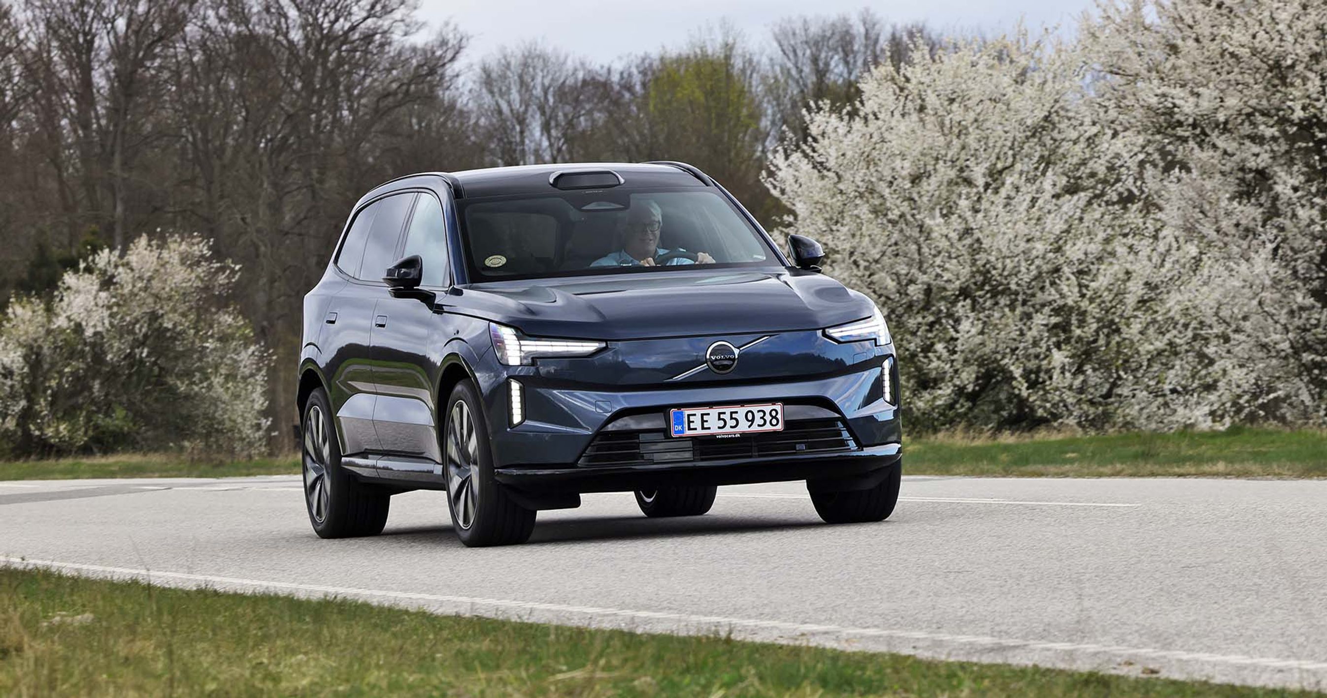 Volvo EX90 kører på vej foran buske med blomster på