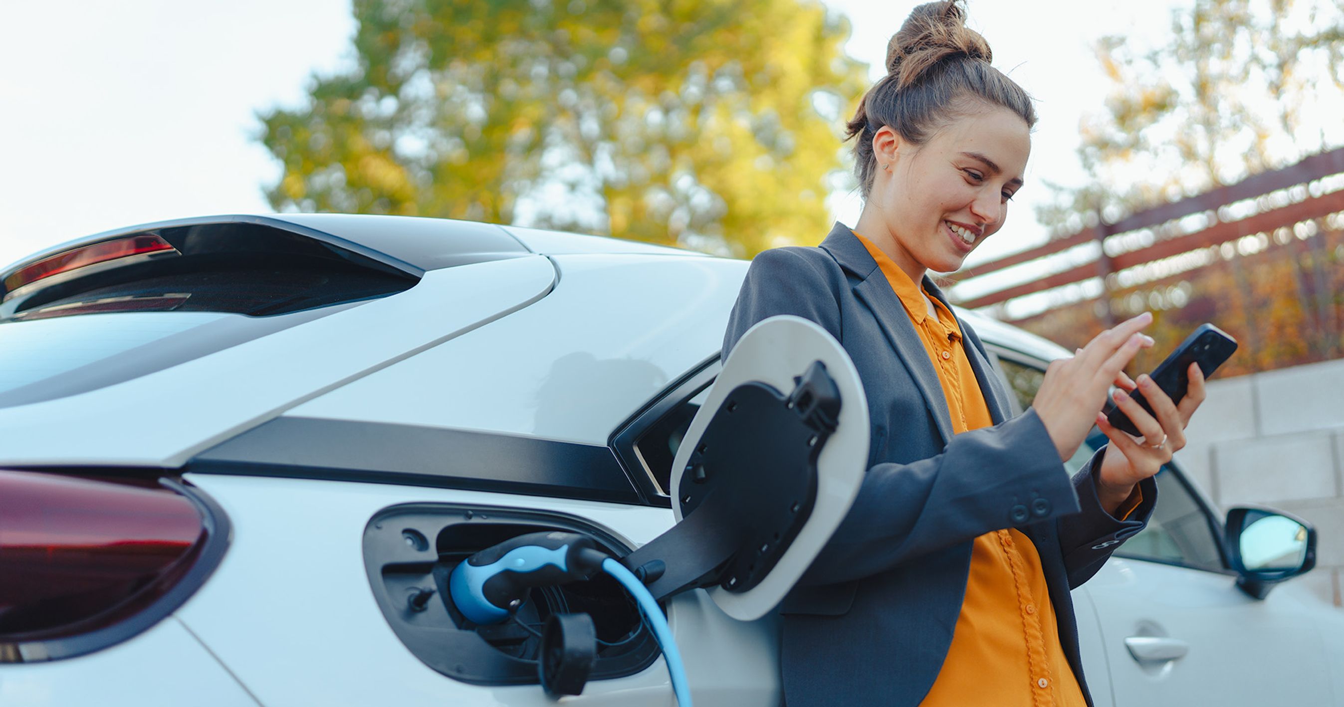 Kvinder står med mobiltelefon ved elbil der lader.