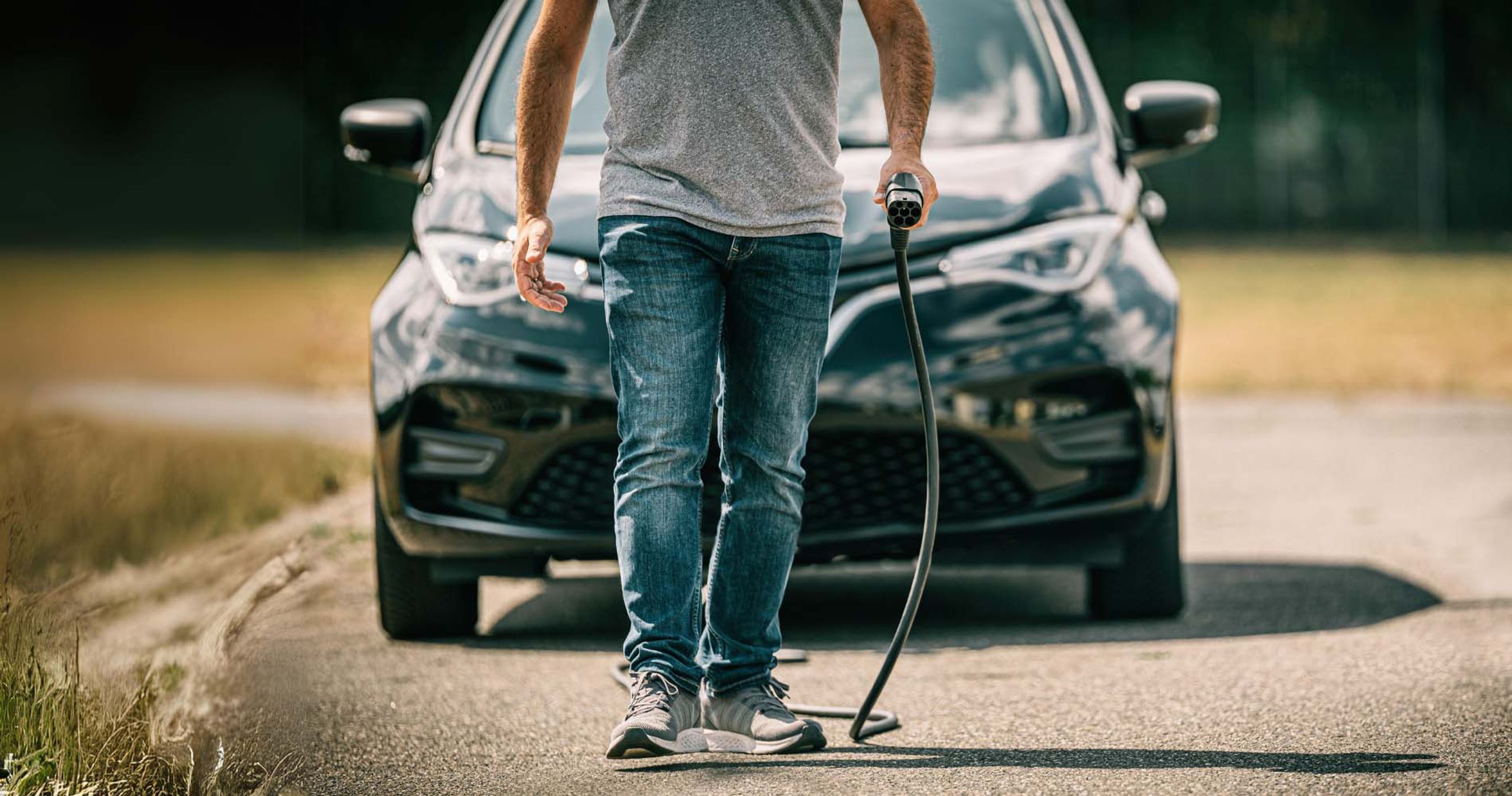 Mand går med ladestik i hånden foran bil