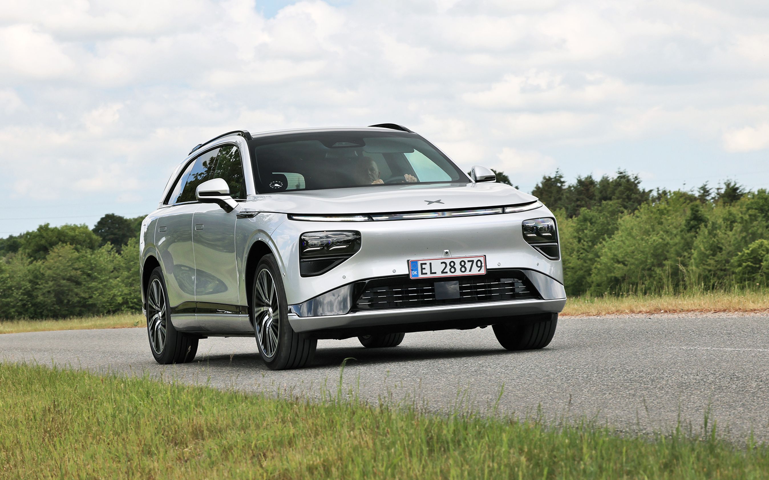Xpeng G9 Standard Range kører på en dansk landevej med grønne træer i baggrunden.