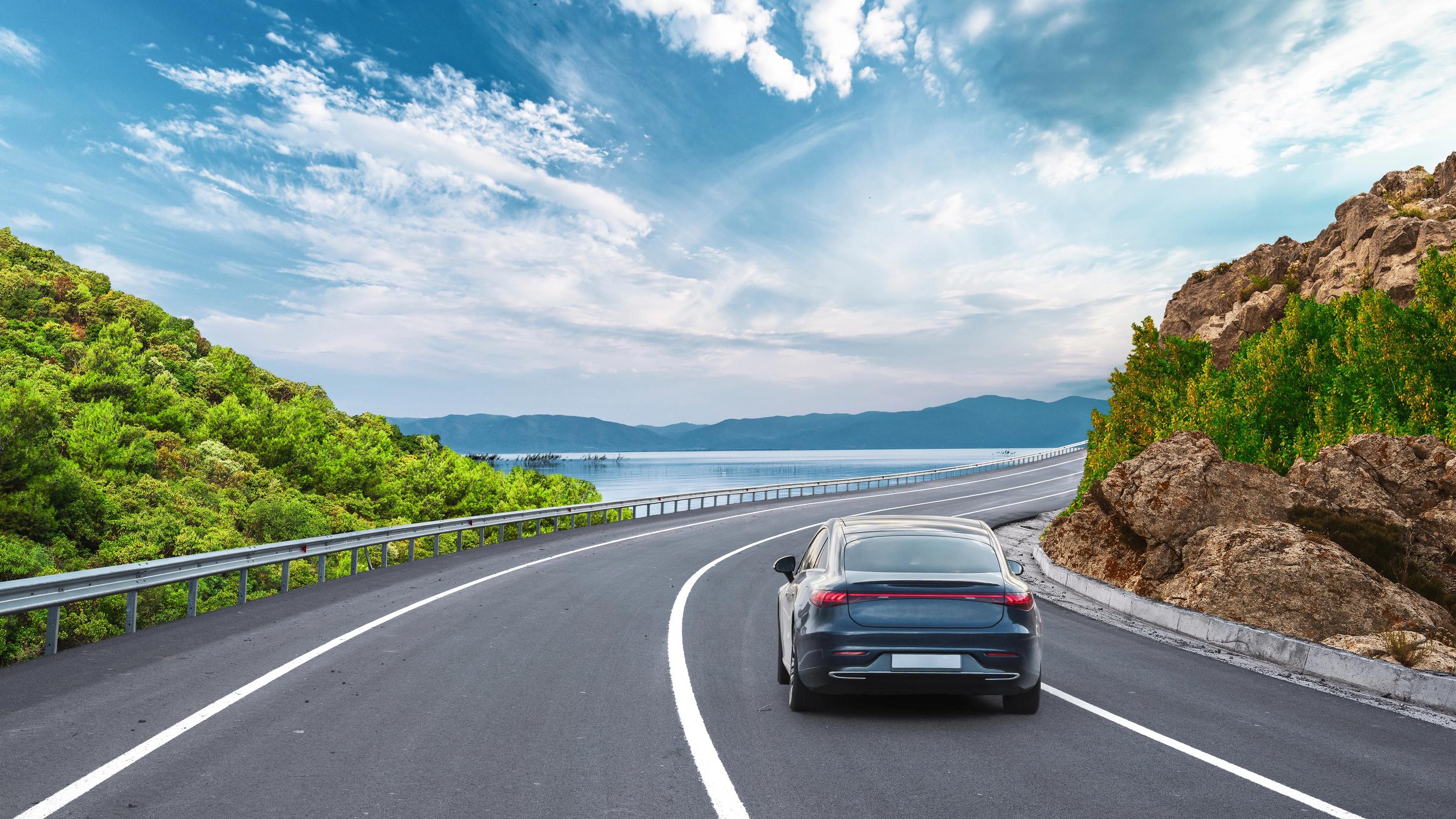 Bil kører på vej ud mod havet. Bjerge i baggrunden.