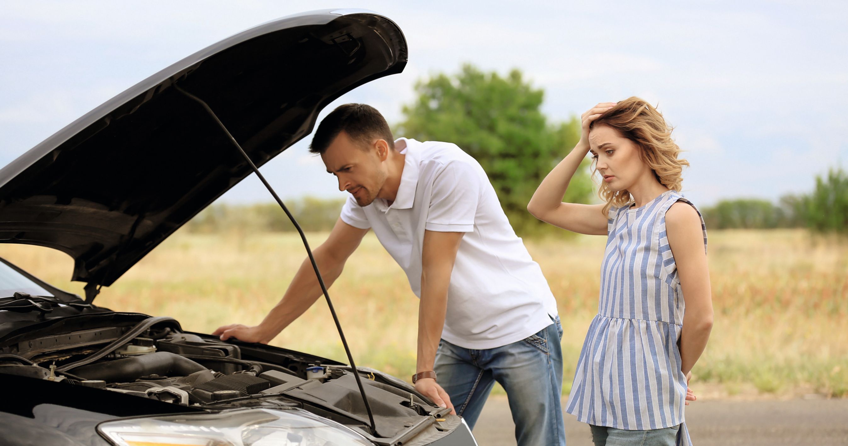 Mand og kvinde står ved en bil med åben kølerhjelm og tager sig til hovedet