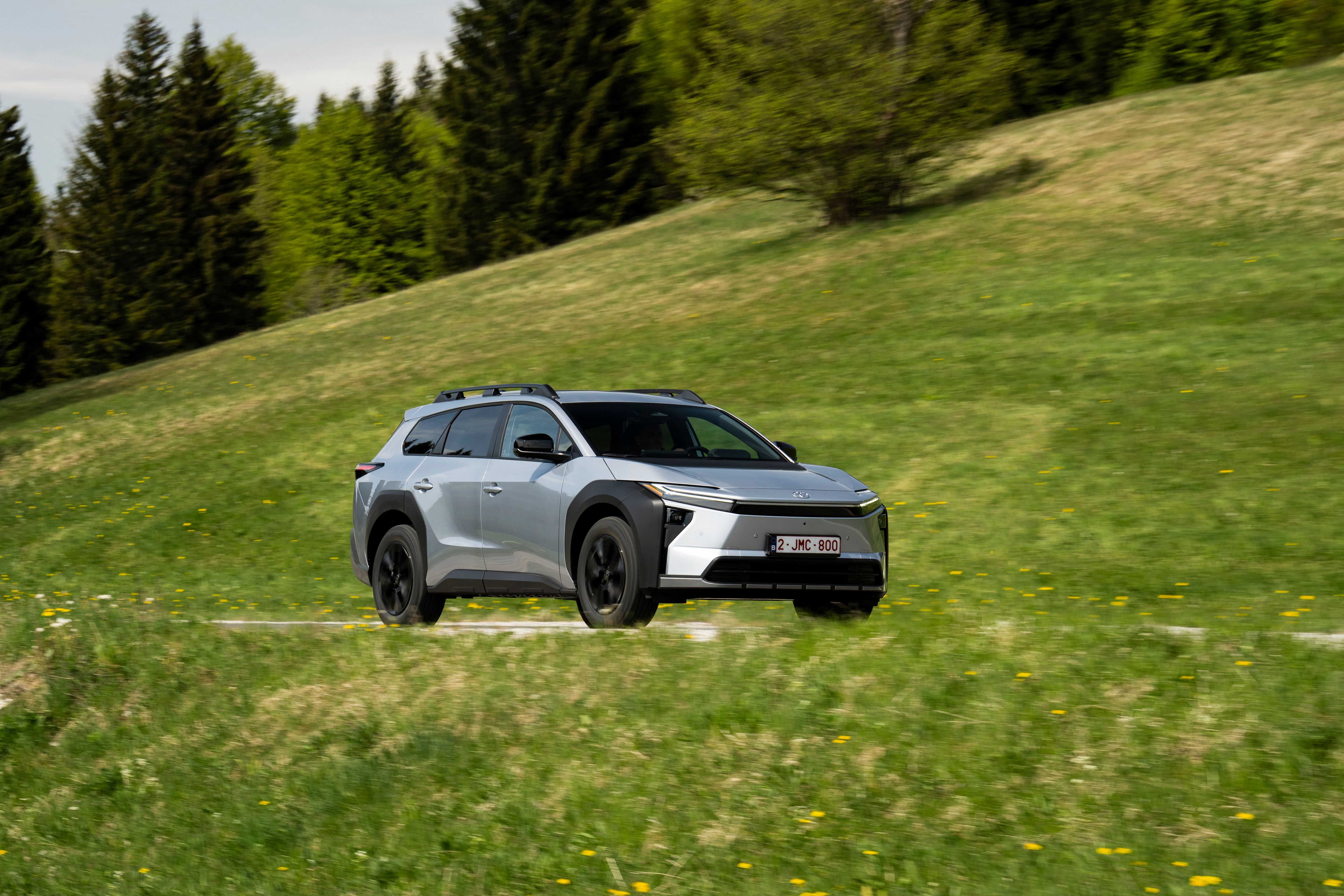 Toyota bZ4X Touring set skråt forfra, mens den kører på bjergvej med græs omkring