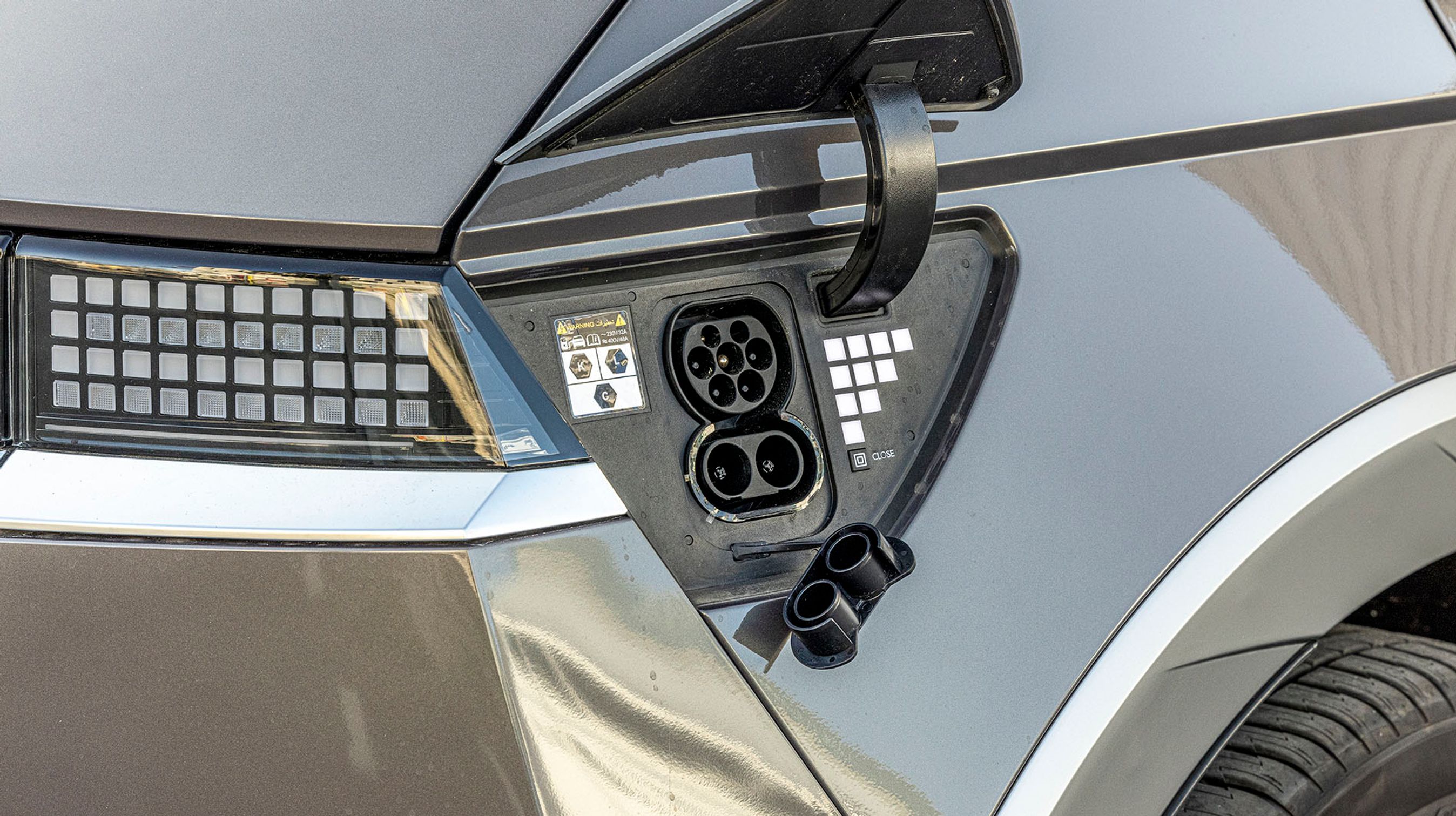 Ladestikket er placeret ved højre baglygte og kan åbnes ved et tryk på dækslet eller via nøglen. Der er et CCS-stik, og hjemme kan den lade med tre faser og 11 kW. På farten med op til 240 kW. De hvide prikker viser, hvor meget strøm der er på batteriet.