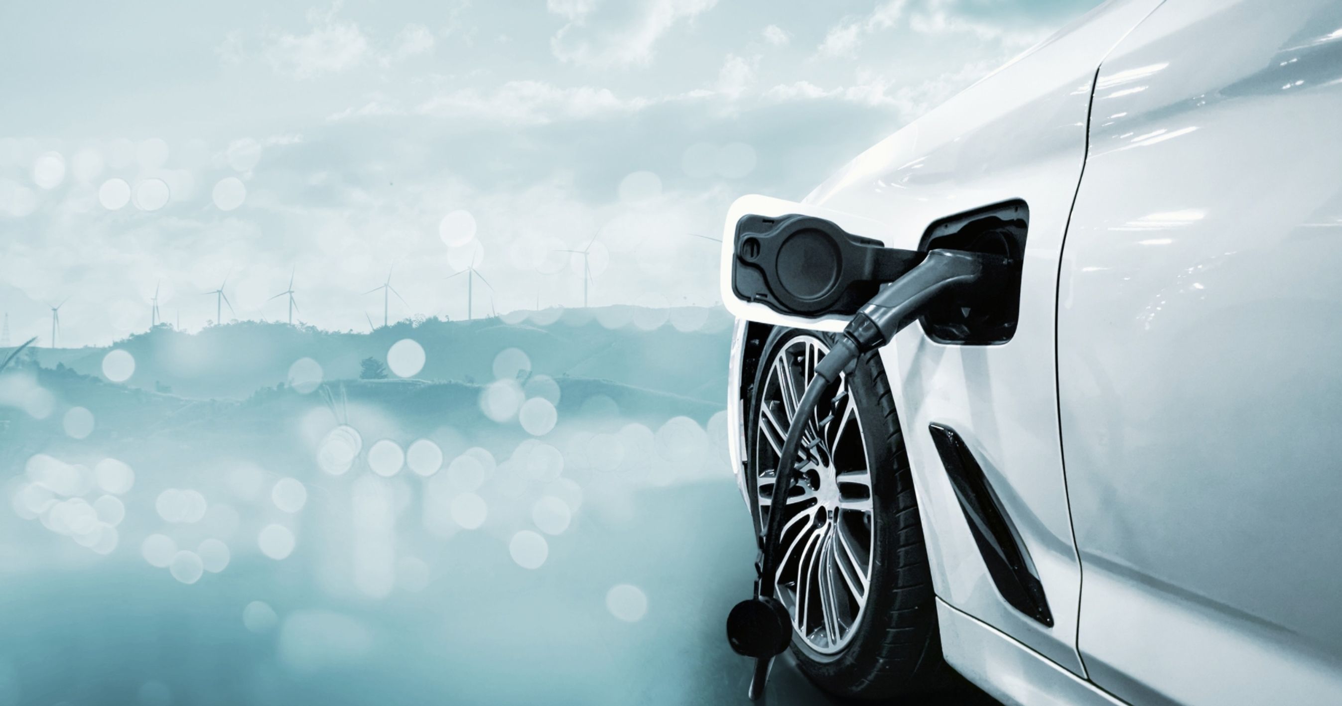 Bil der bliver opladet. Vindmøller i baggrunden.