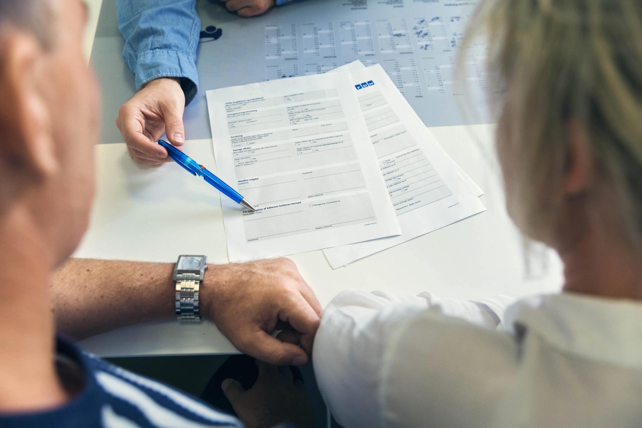 Billede af personer, der ser på papirer og bliver rådgivet.