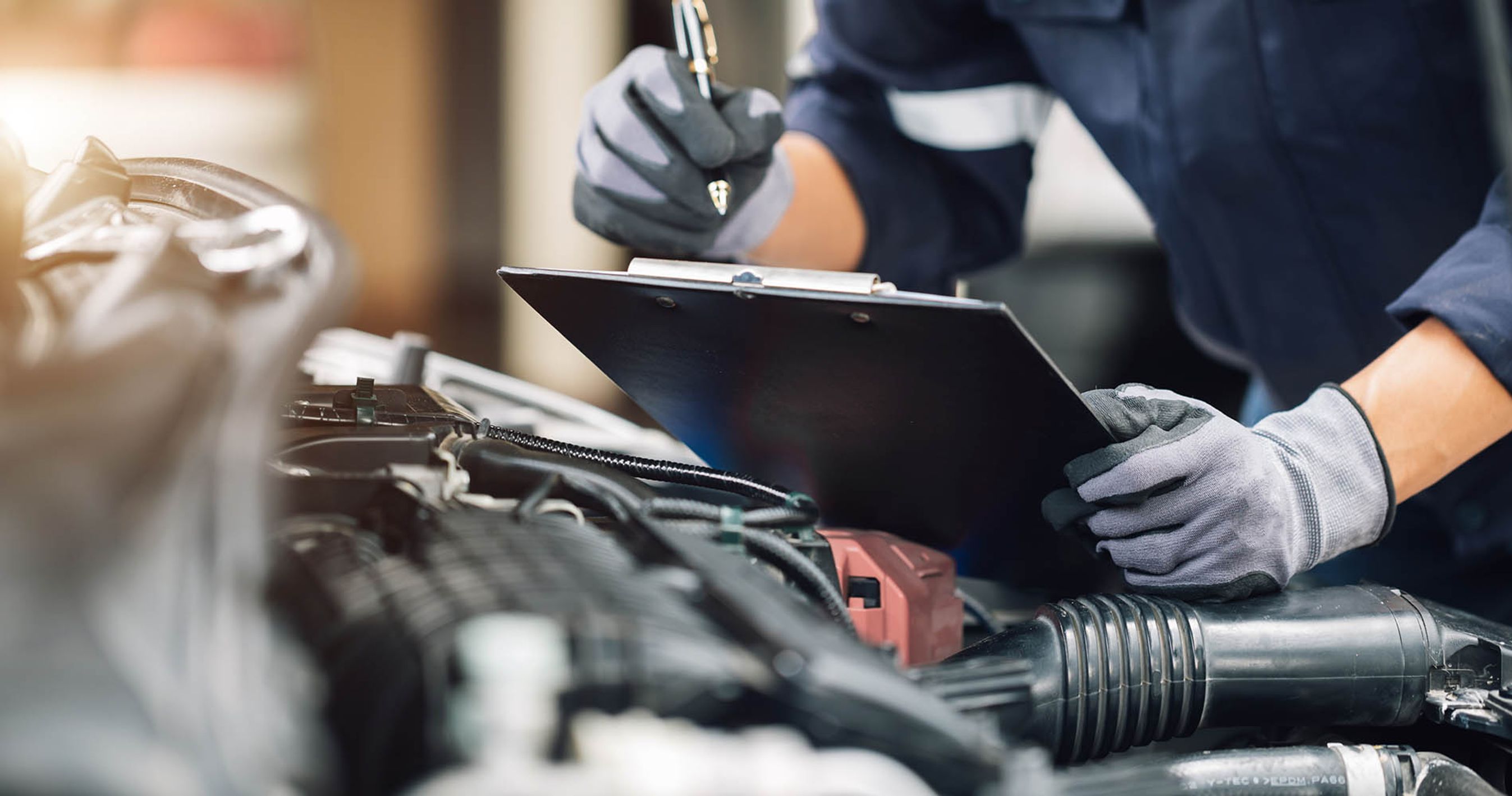 Mekaniker tager noter under serviceeftersyn. Motor kan ses i forgrunden. 