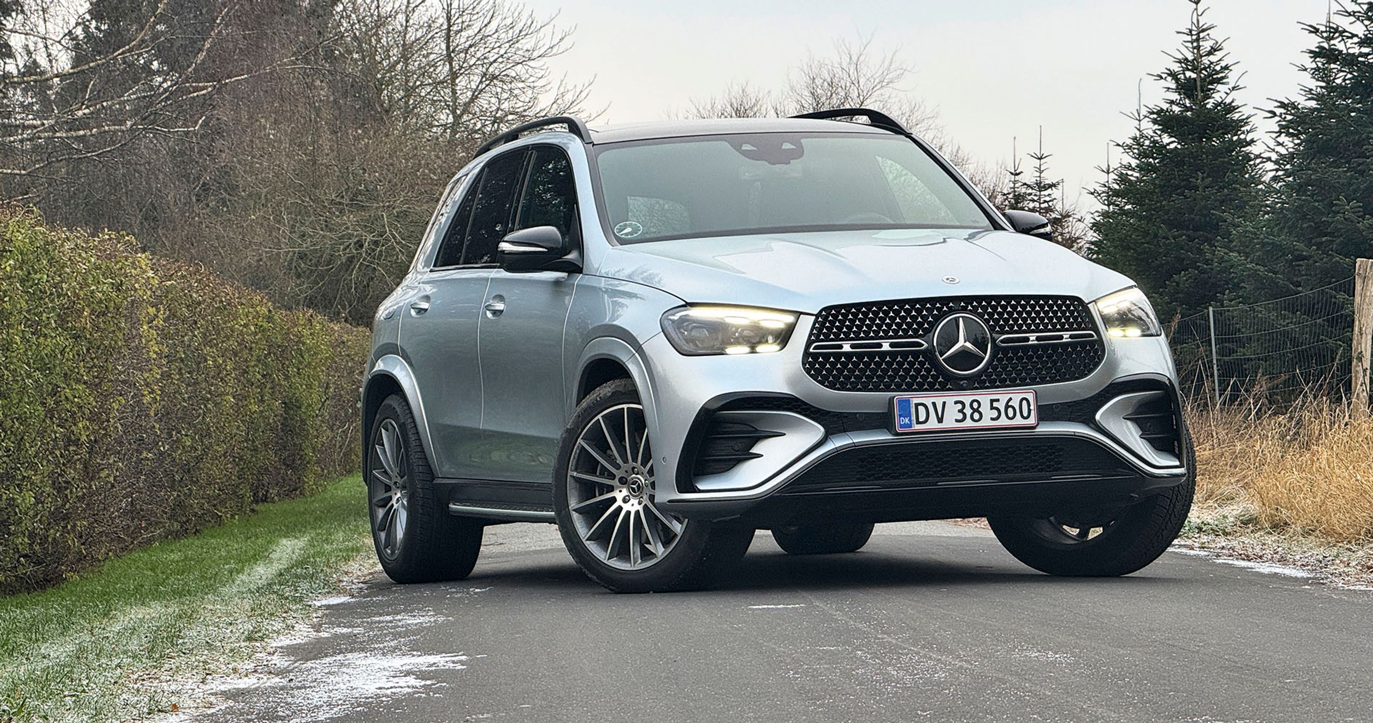 En sølvgrå Mercedes-Benz GLE holder på en vej med en hæk i baggrunden.