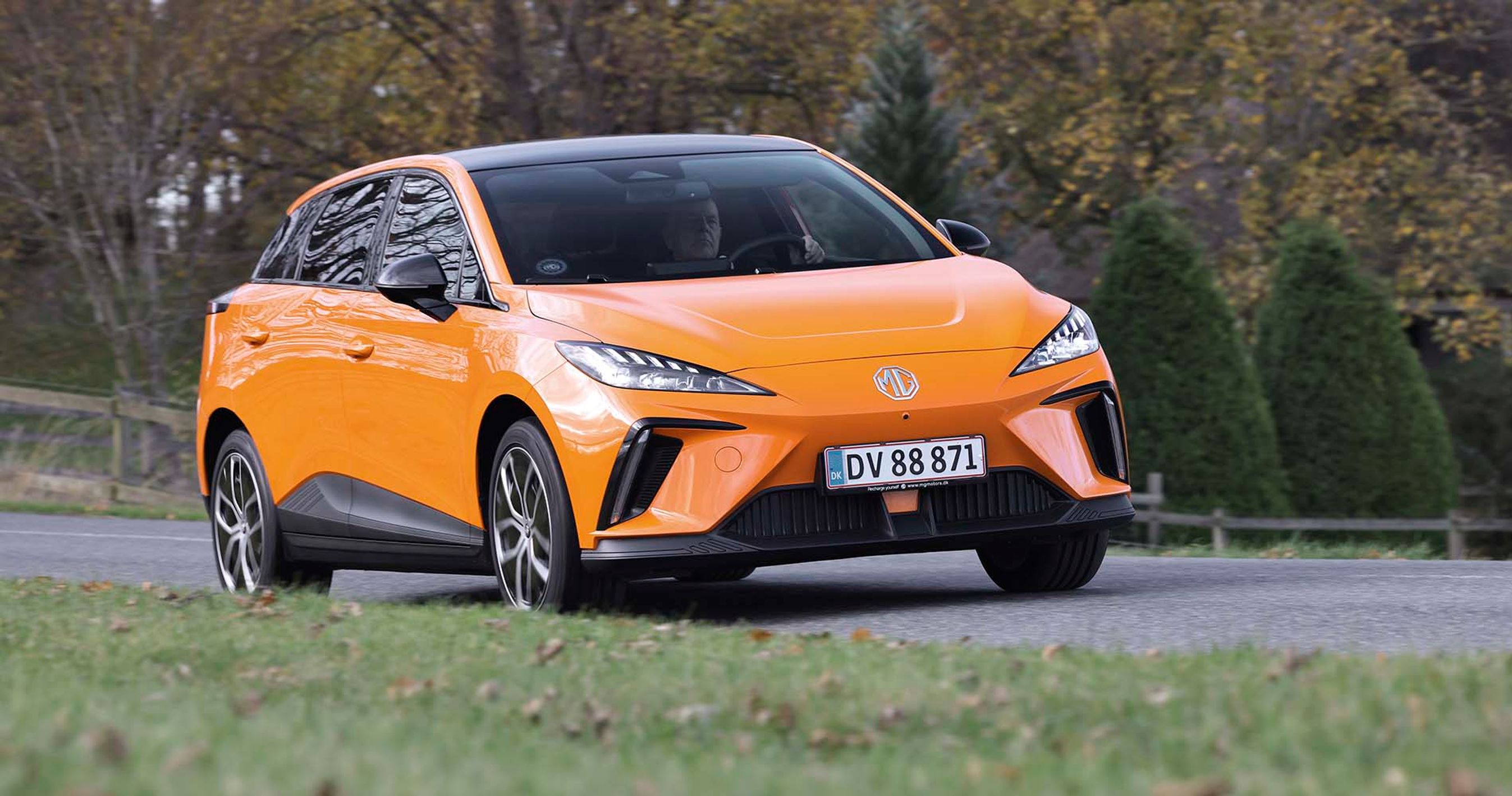 En orange MG 4 kører på en vej med træer i baggrunden