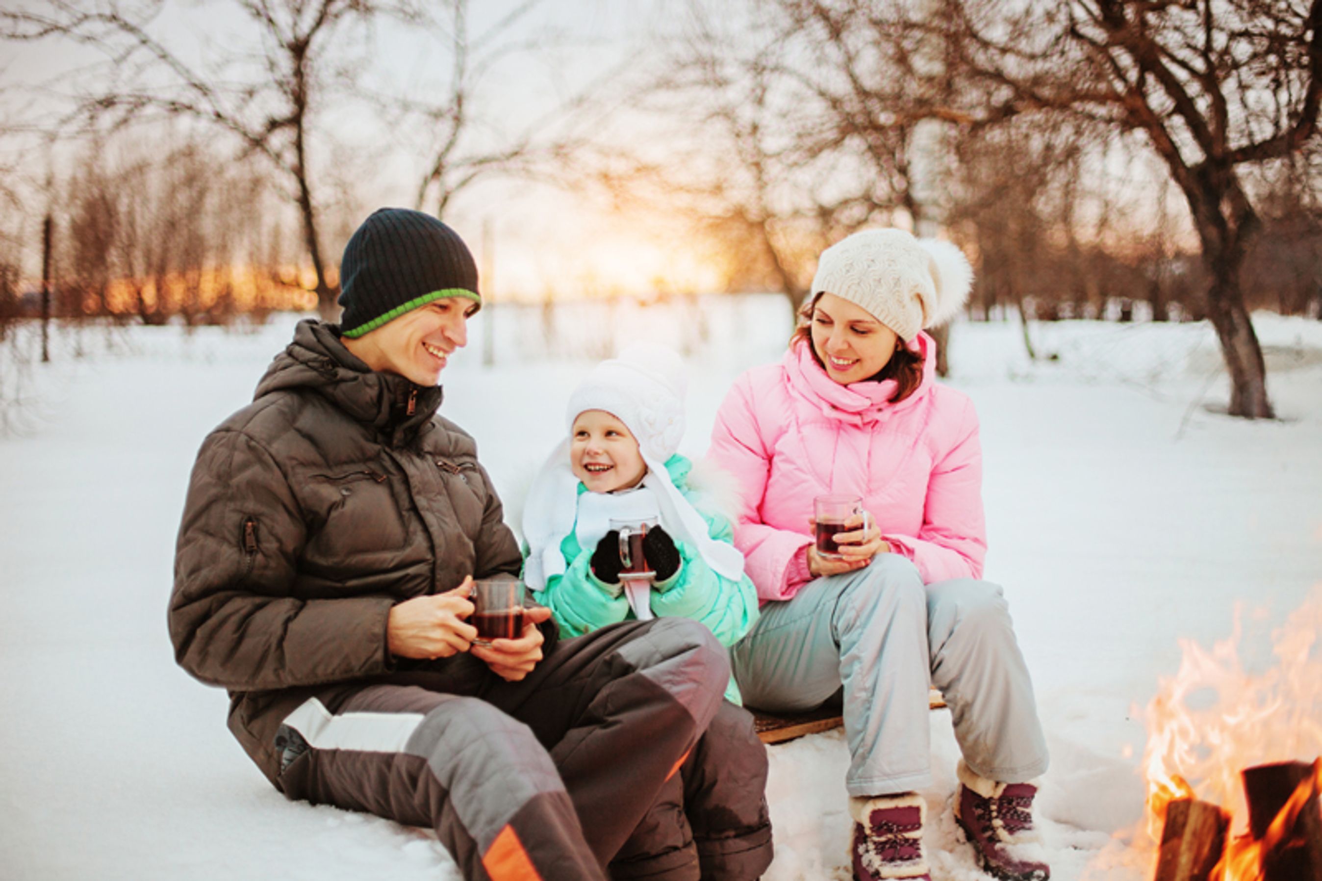 en familie sidder sammen i sne med noget varmt at drikke