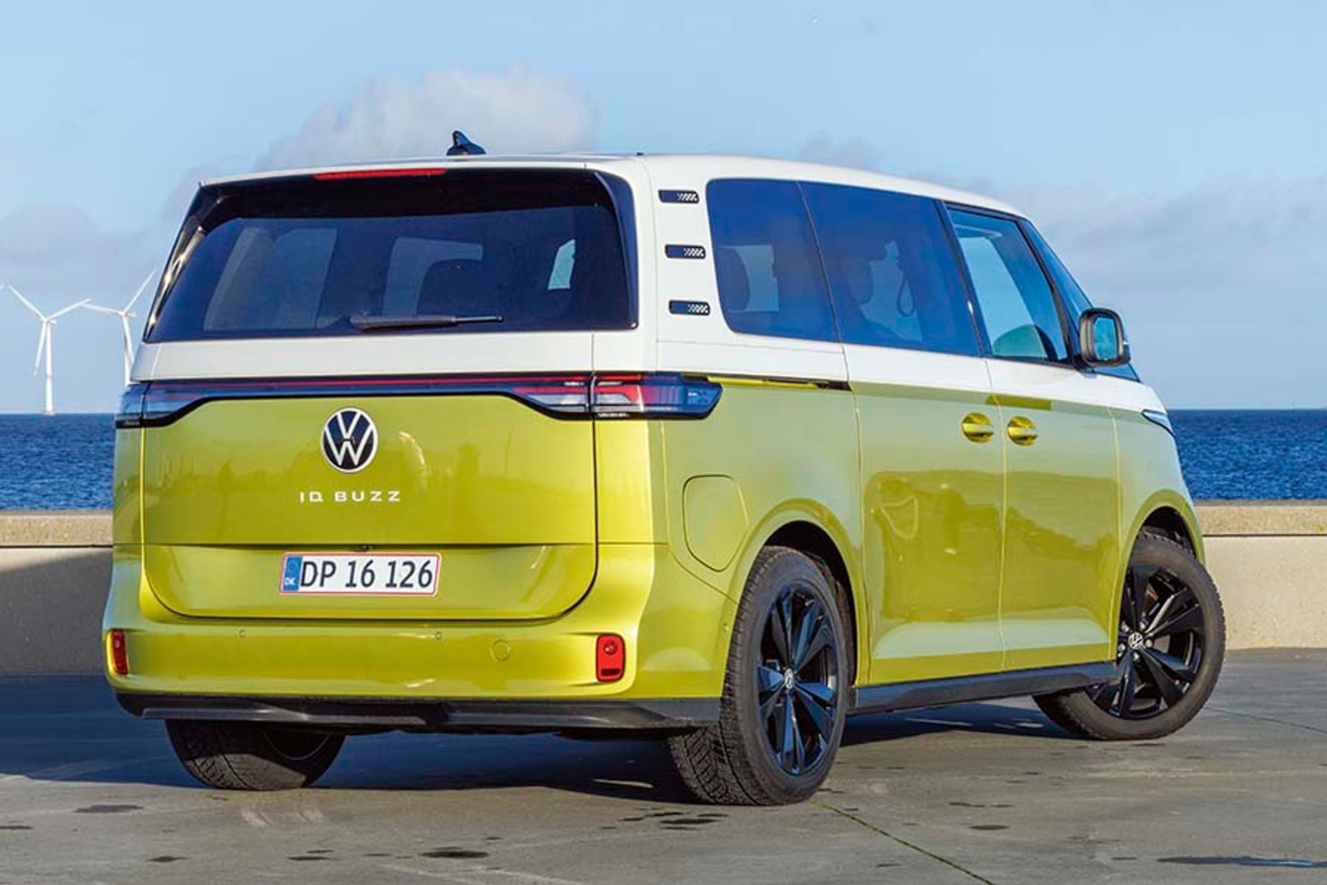 VW ID. Buzz set bagfra, mens den står på Amager Strandpark med vindmøller i baggrunden