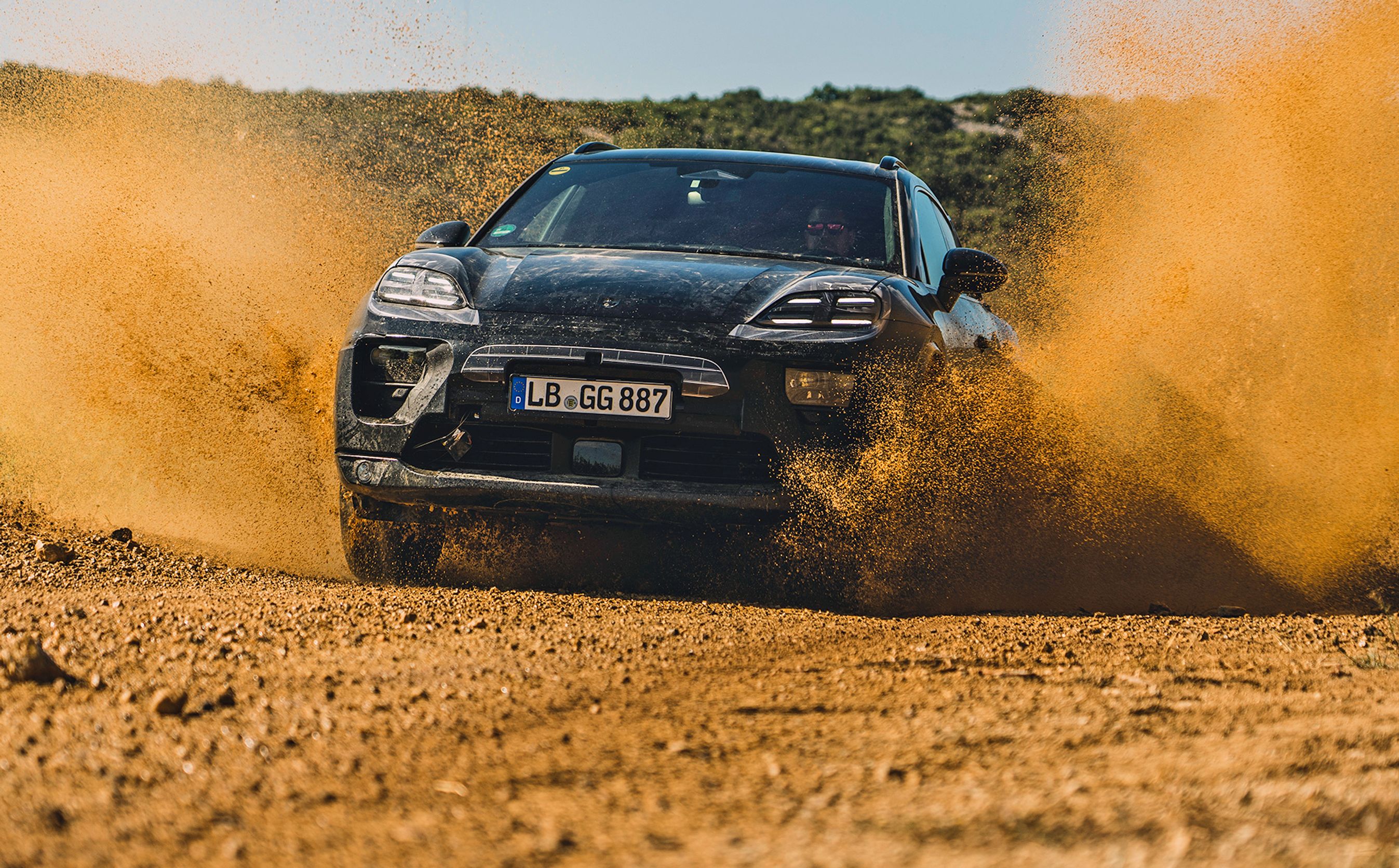Porsche Macan forfra med sand, der flyver op fra hjulene.