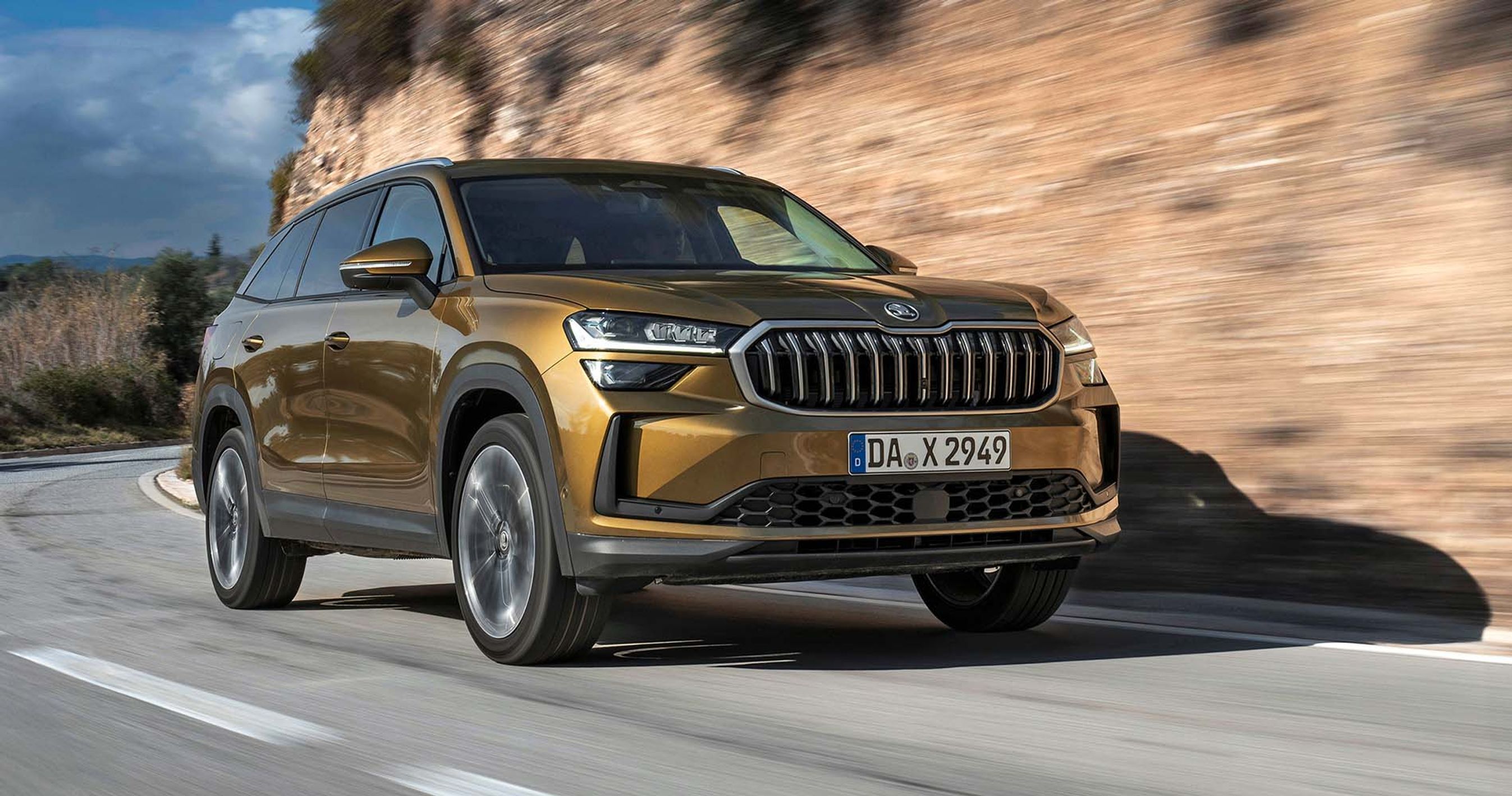 Guldfarvet Skoda Kodiaq kører i sving med bjerg i baggrunden
