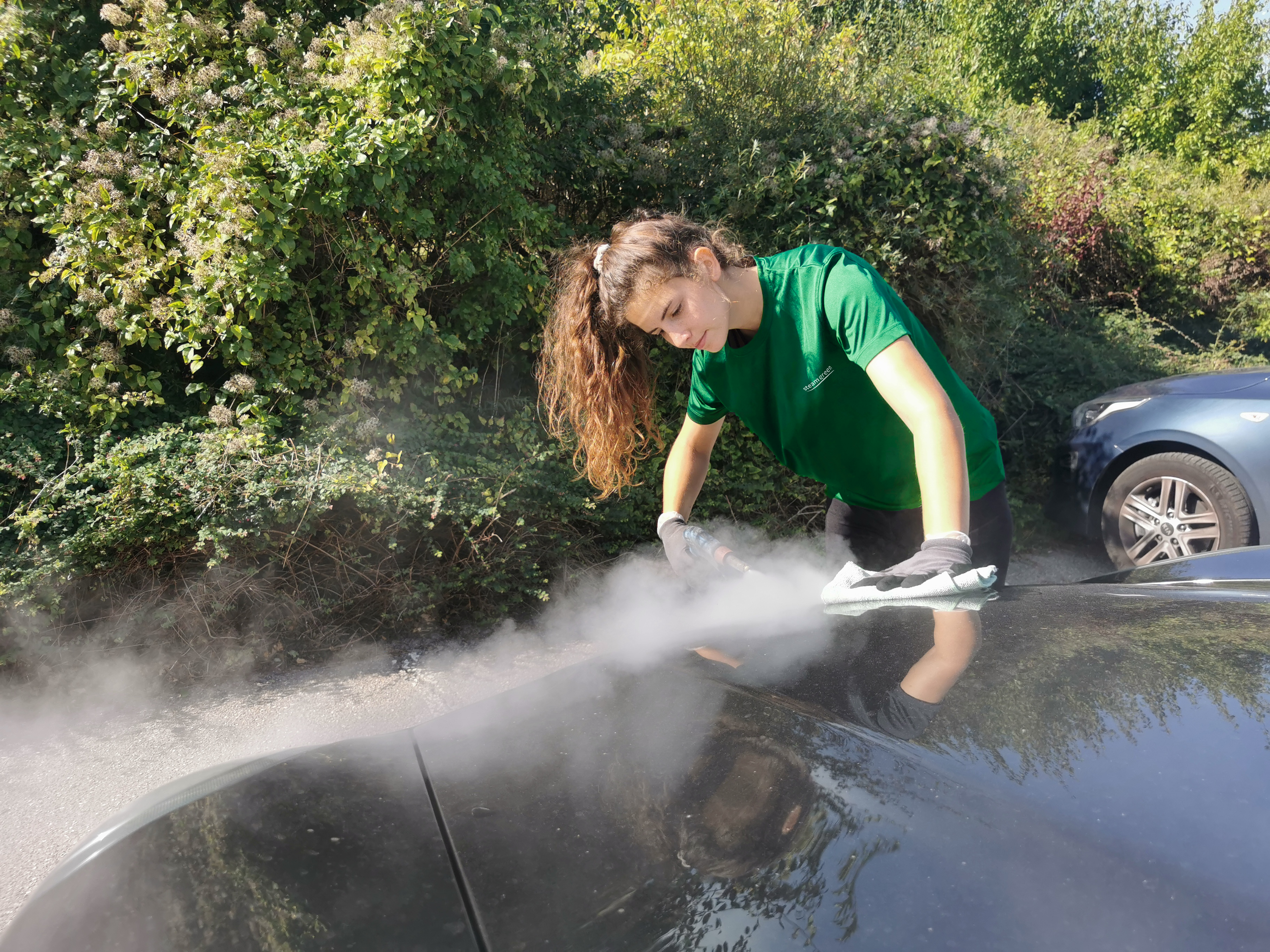 Kvindelig medarbejder hos SteamGreen renser bil med damp i solskin