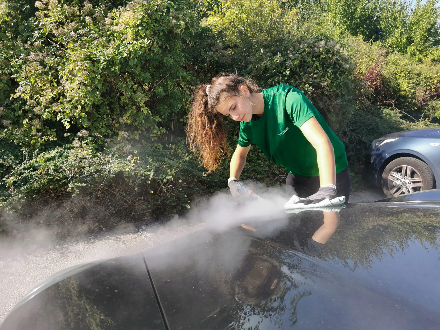 Kvindelig medarbejder hos SteamGreen renser bil med damp i solskin