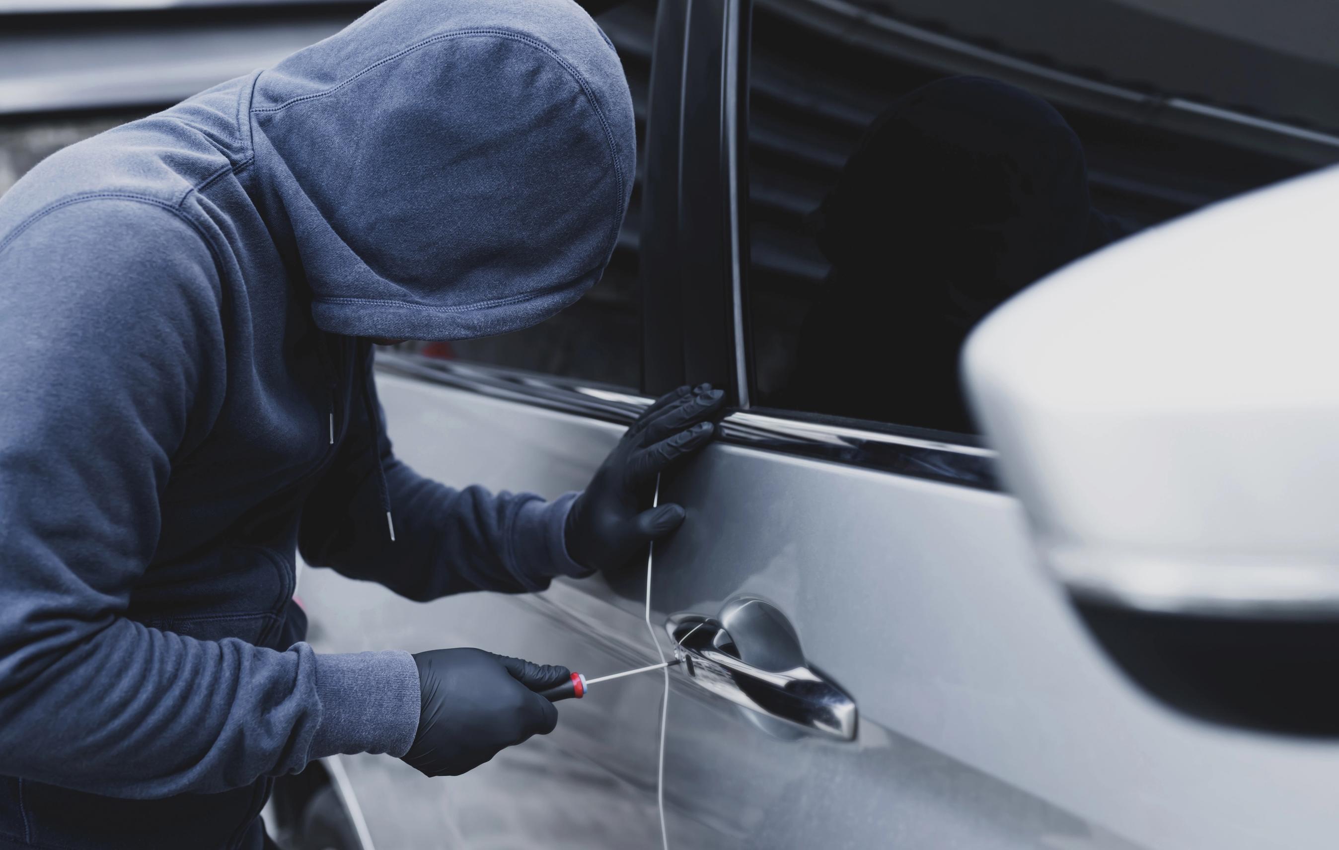 Hætteklædt person forsøger at bryde ind i en bil ved at få den ene dør brudt op.