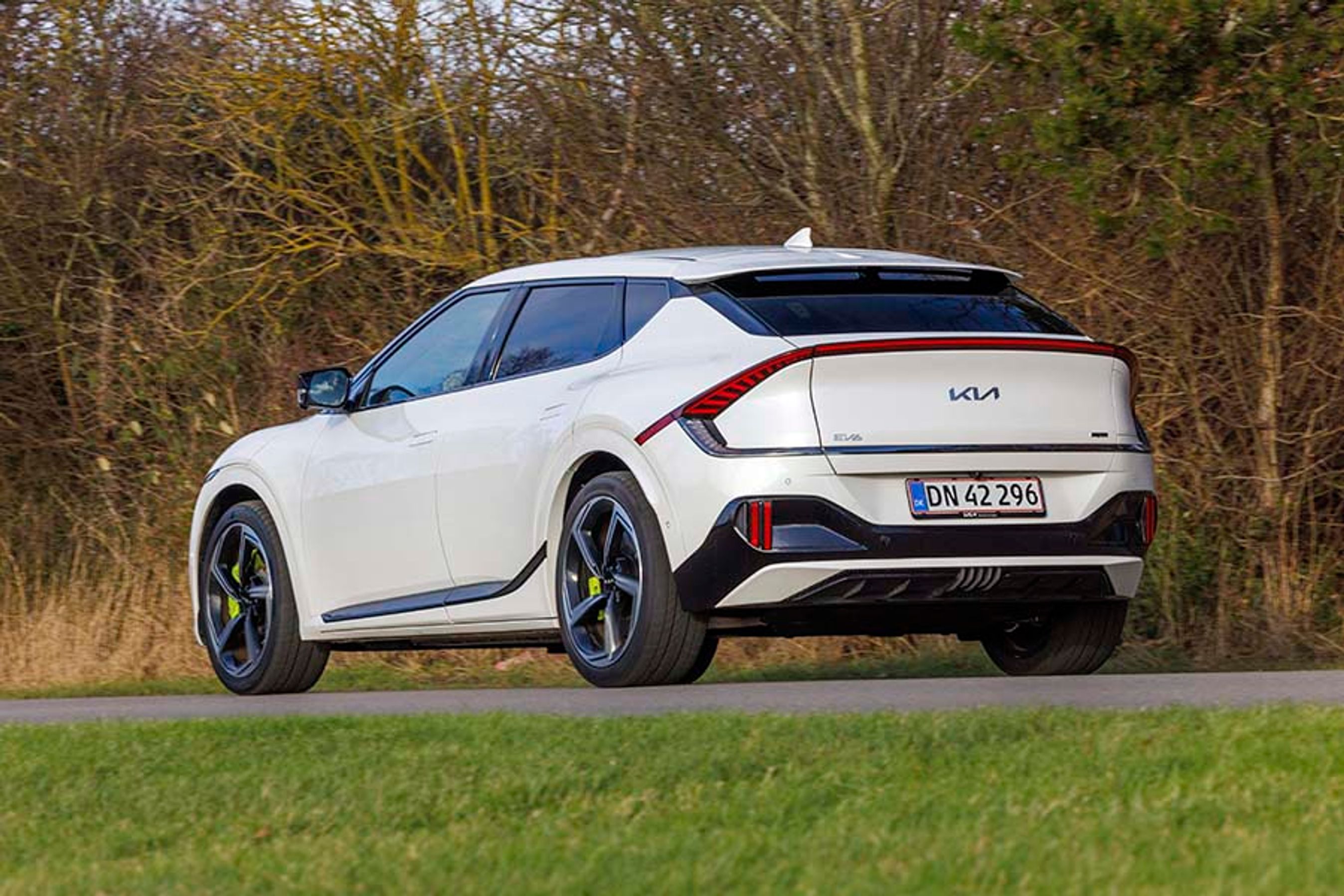 En hvid KIa EV& GT set bagfra, mens den kører på en landevej med træer i baggrunden