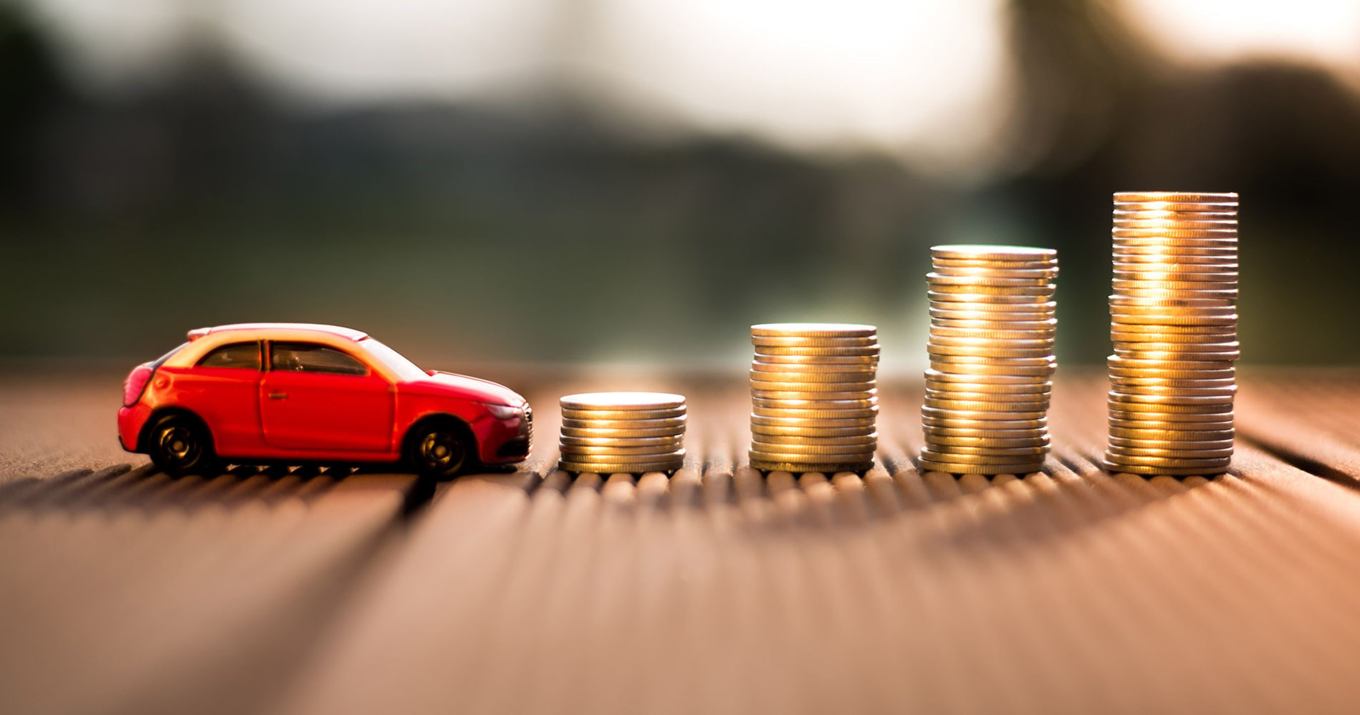 Lille rød modelbil holder foran fire stabler med mønter