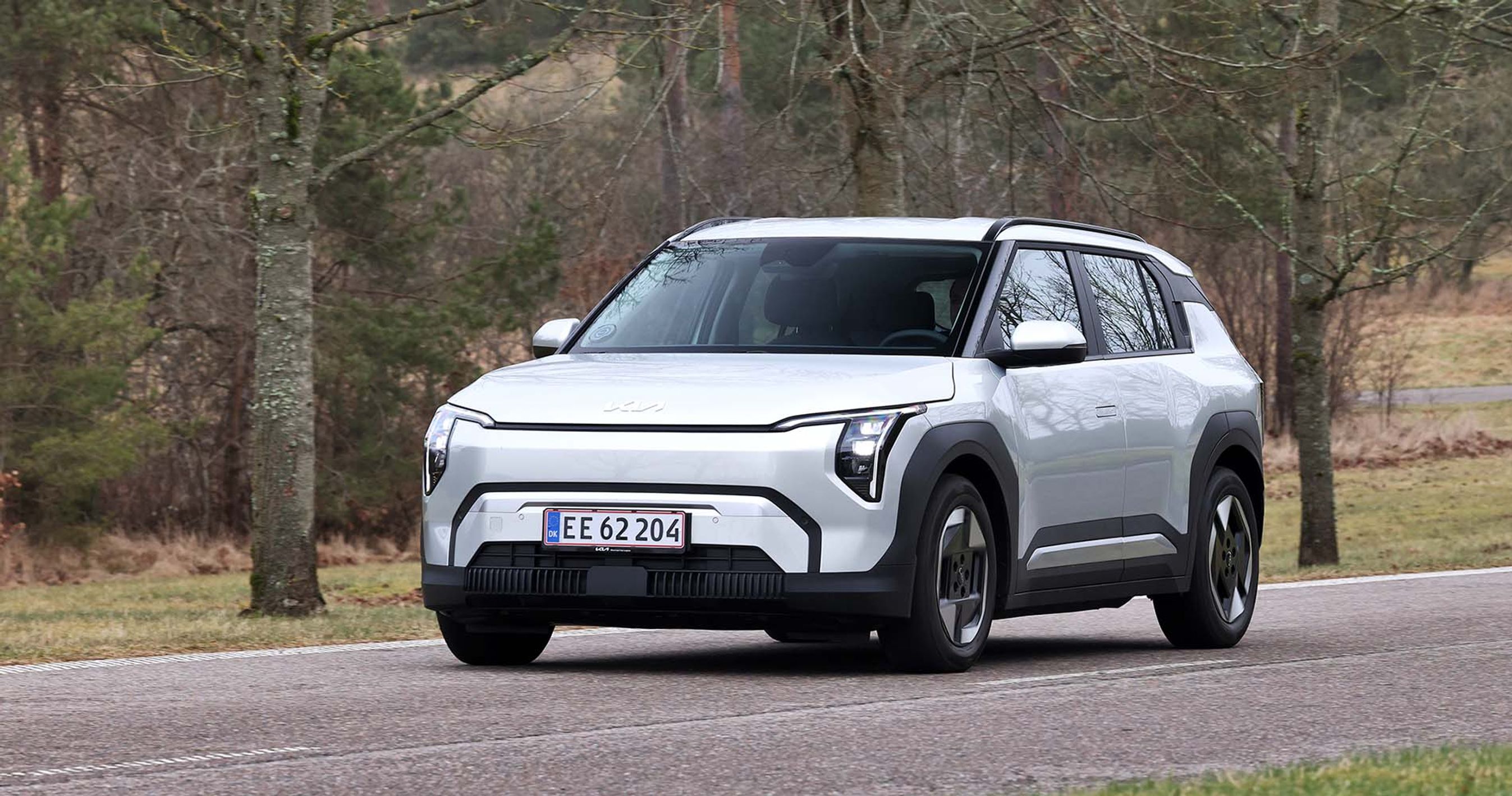 Kia EV3 set skråt forfra, mens den kører på vej mellem træer