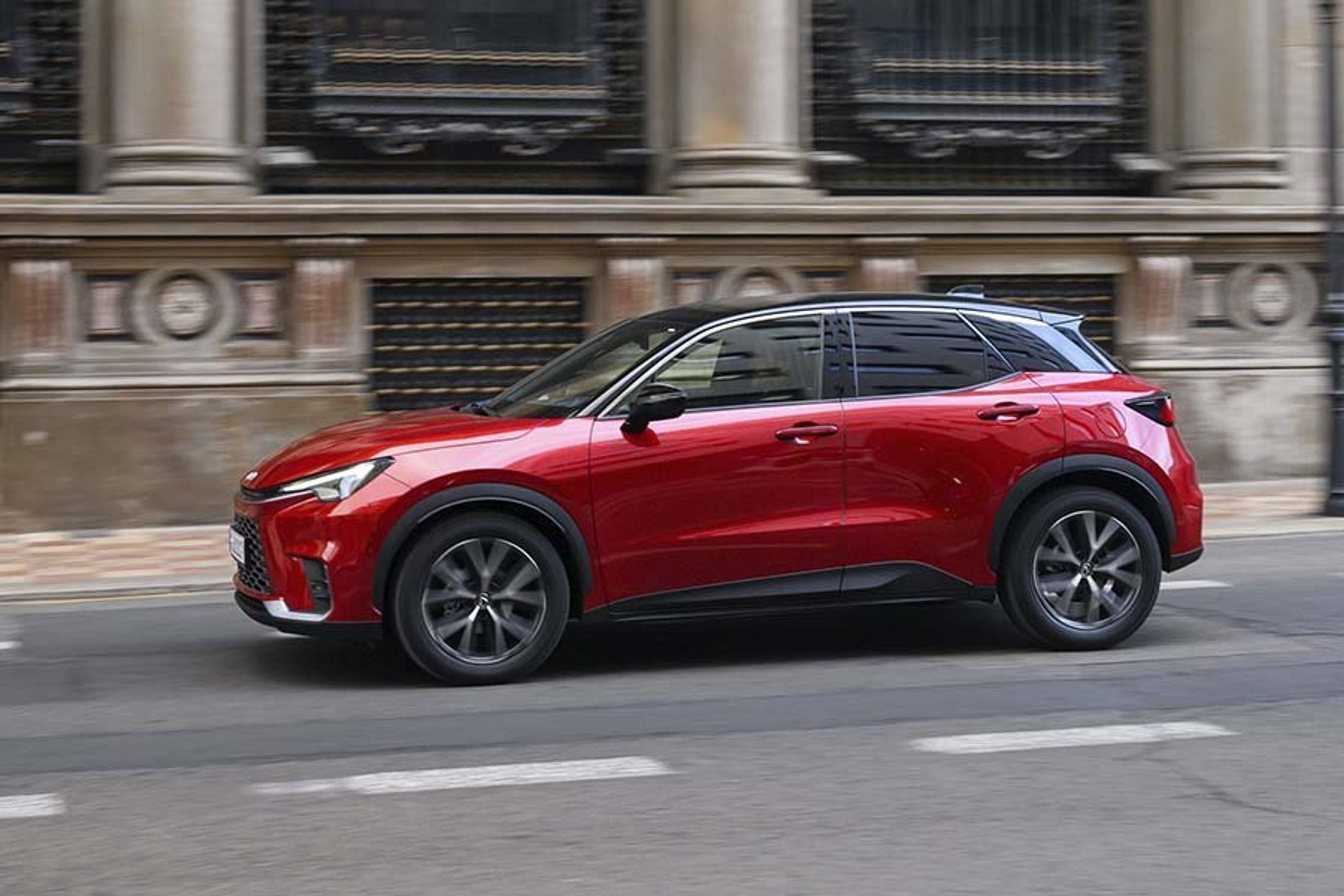 En rød Lexus LBX set fra siden, mens den kører foran en bygning