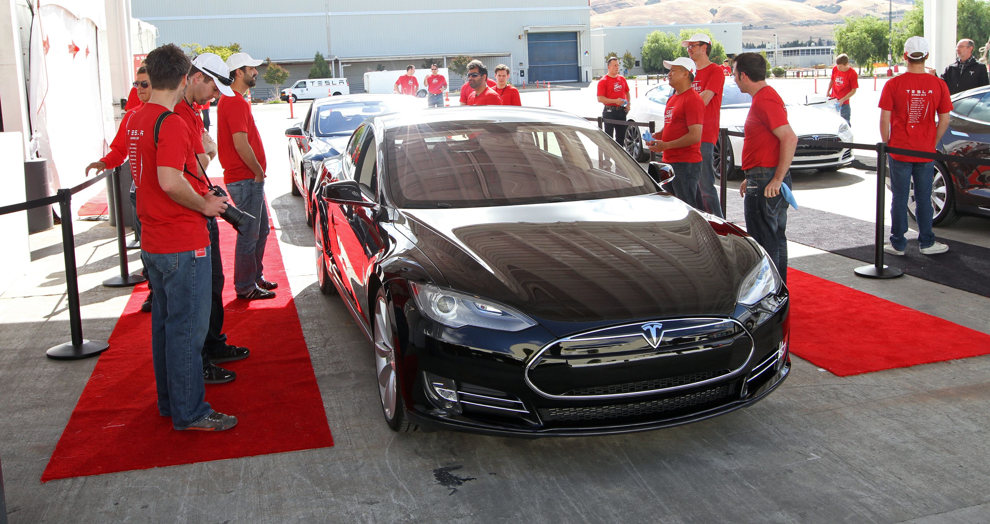 Sort bil på rød løber med folk omkring.