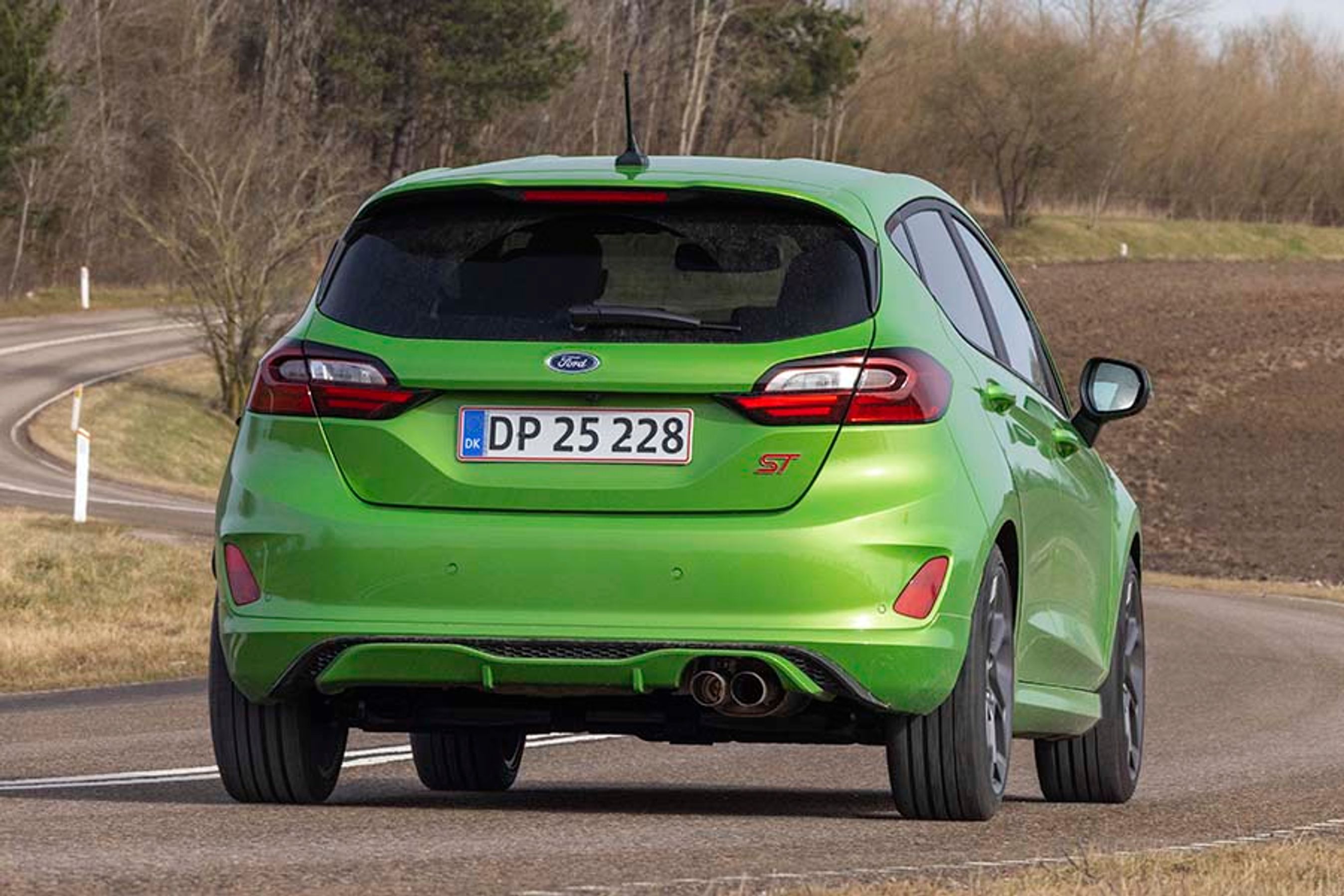 Grøn Ford Fiesta set bagfra, mens den kører på en landevej