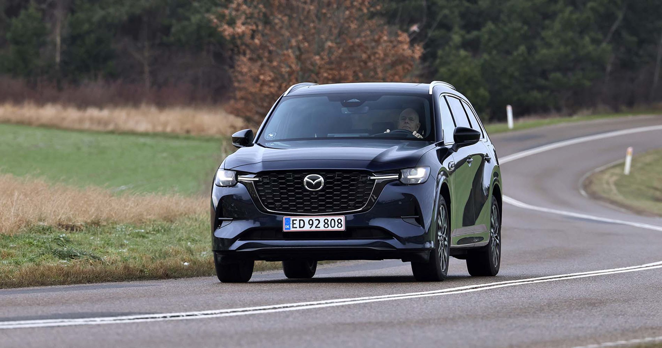 Mazda CX-80 set forfra kører i et sving på en landevej