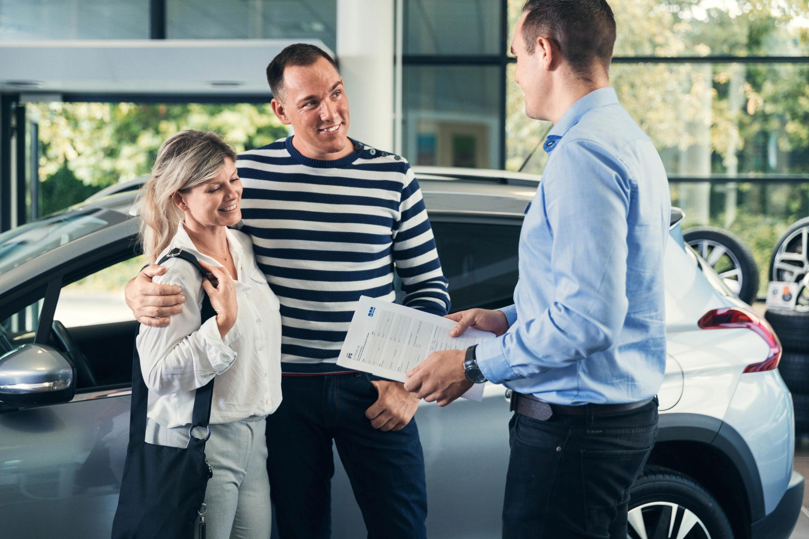 Et par står over for en bilforhandler, som holder en bunke papirer.