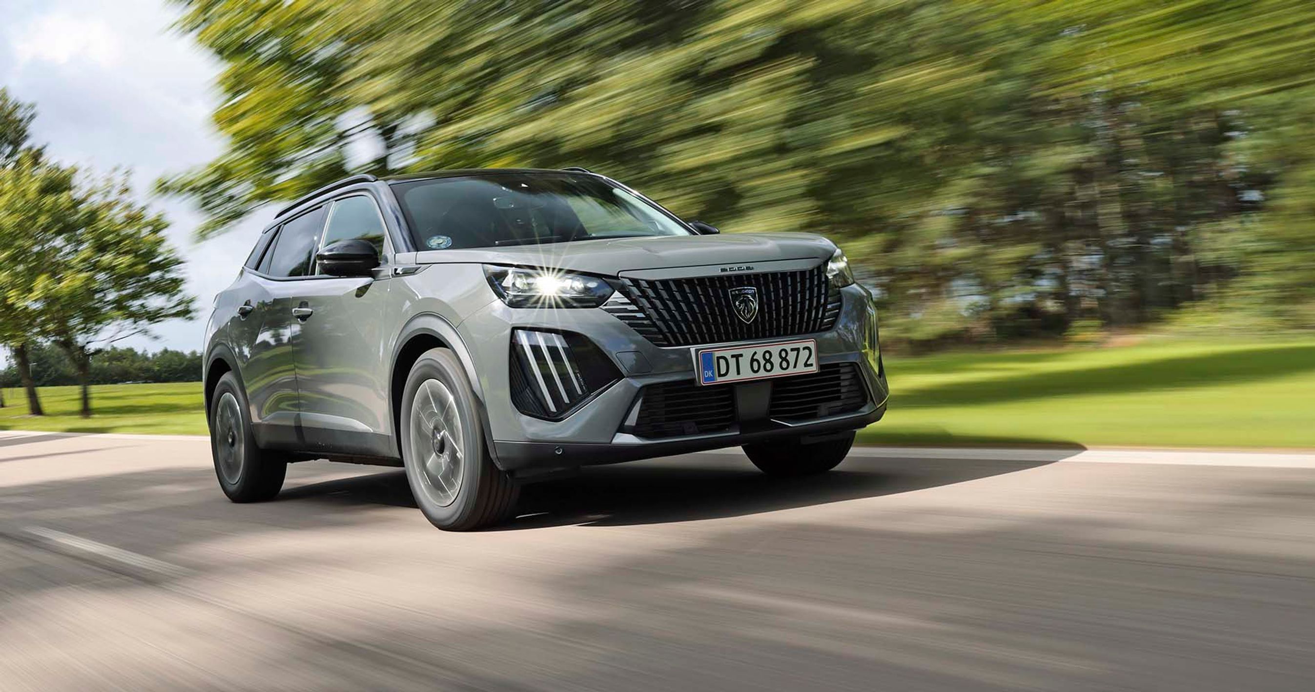 Elbilen Peugeot E-2008 set forfra, mens den kører hurtigt med træer i baggrunden.