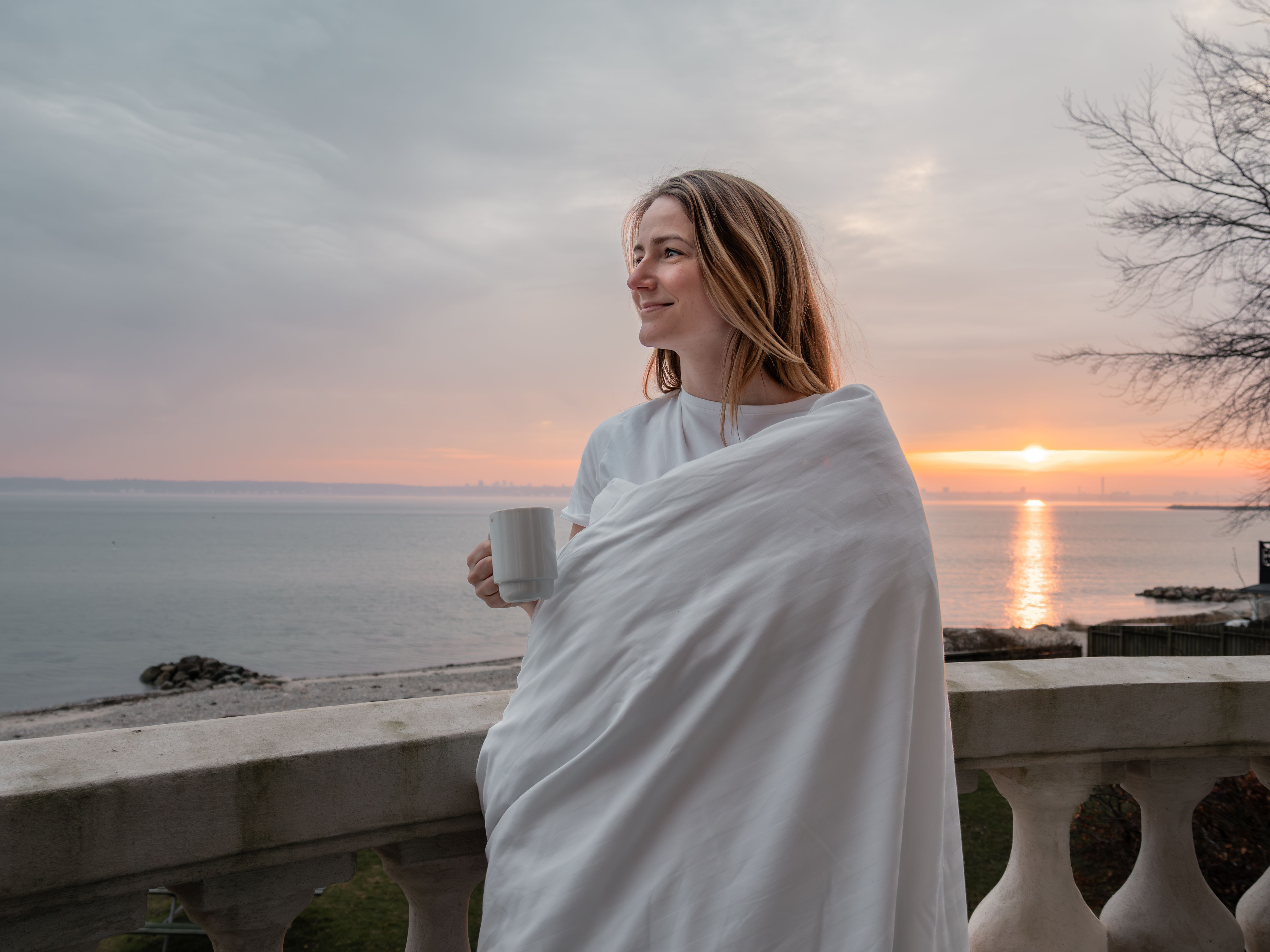 Danhostel - kvinde nyder solopgang på smuk balkon med usigt til vand
