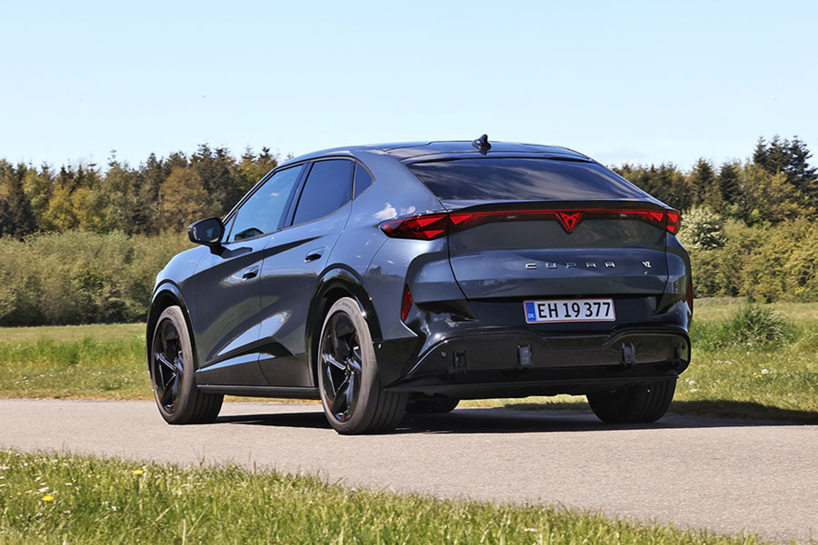 Cupra Tavascan set bagfra, mens den kører på en vej med træer i baggrunden