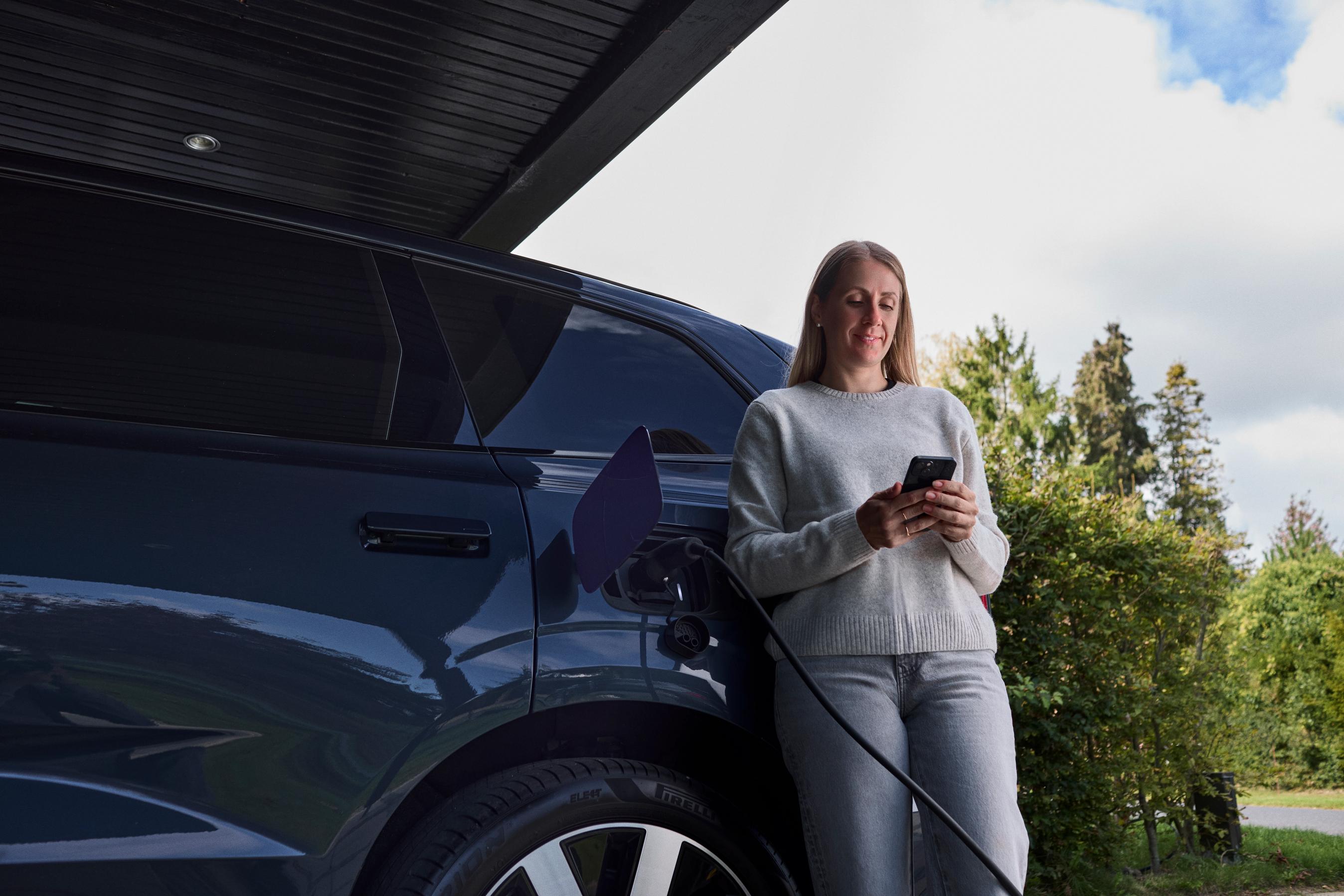 Kvinde står og kigger på FDM ladeløsninger, mens hendes bil lader i garagen