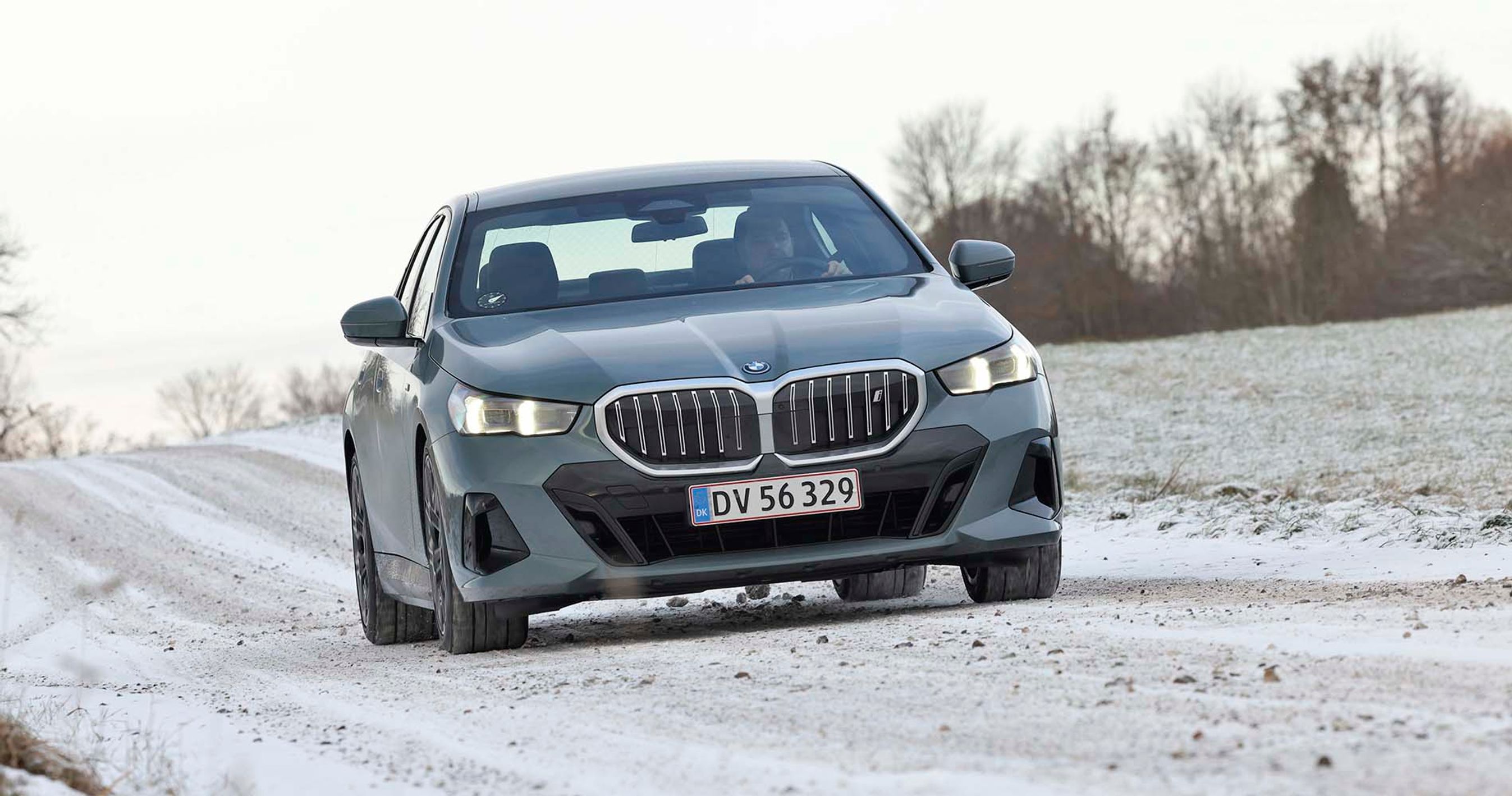 En BMW i5 elbil set forfra kører på en snedækket vej i et snedækket landskab.