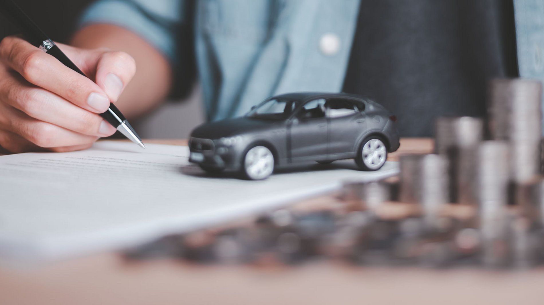 Mand skriver på et stykke papir. Modelbil står på papiret og ved siden af er der en stabel med mønter.