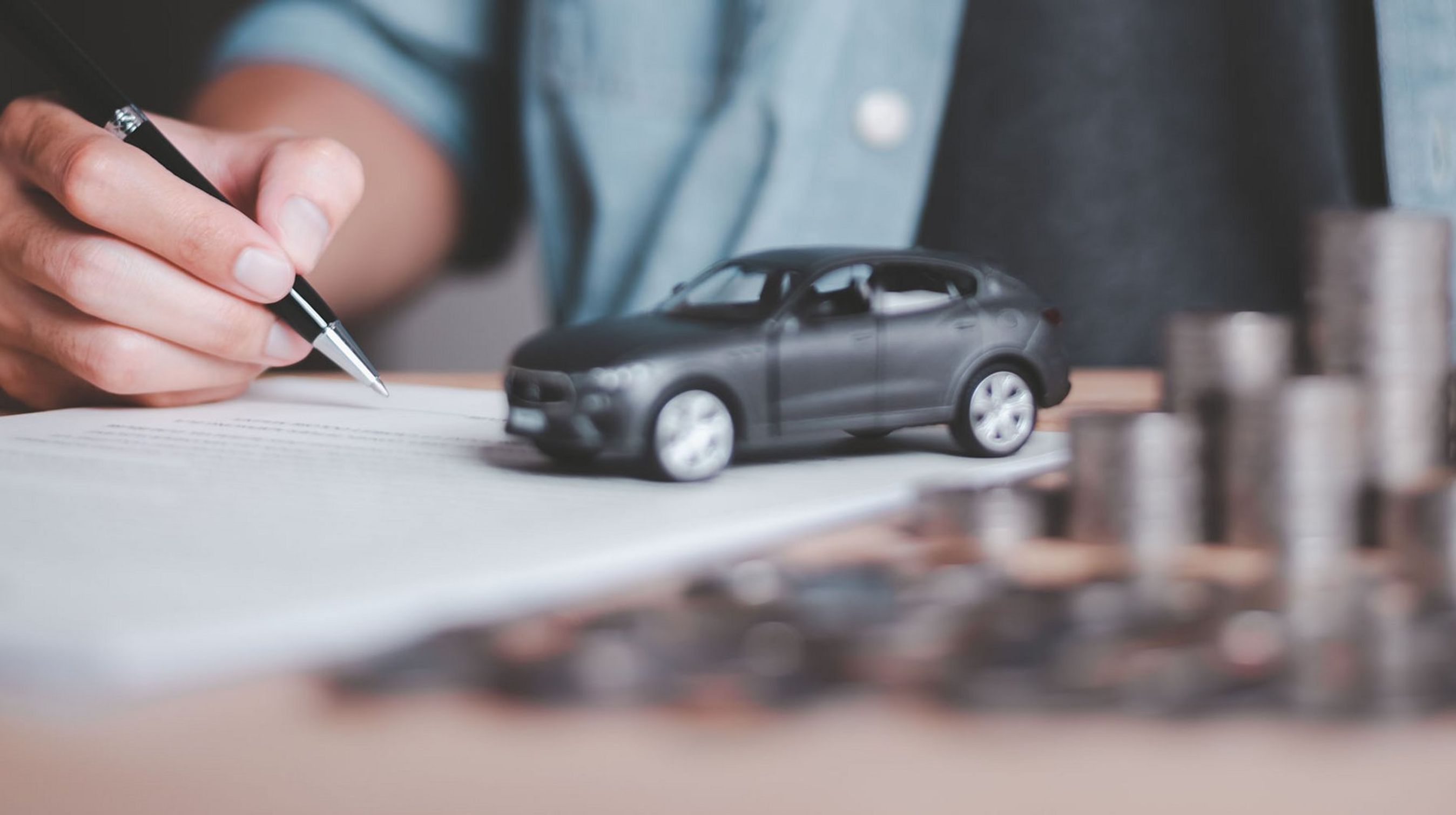 Mand skriver på et stykke papir. Modelbil står på papiret og ved siden af er der en stabel med mønter.