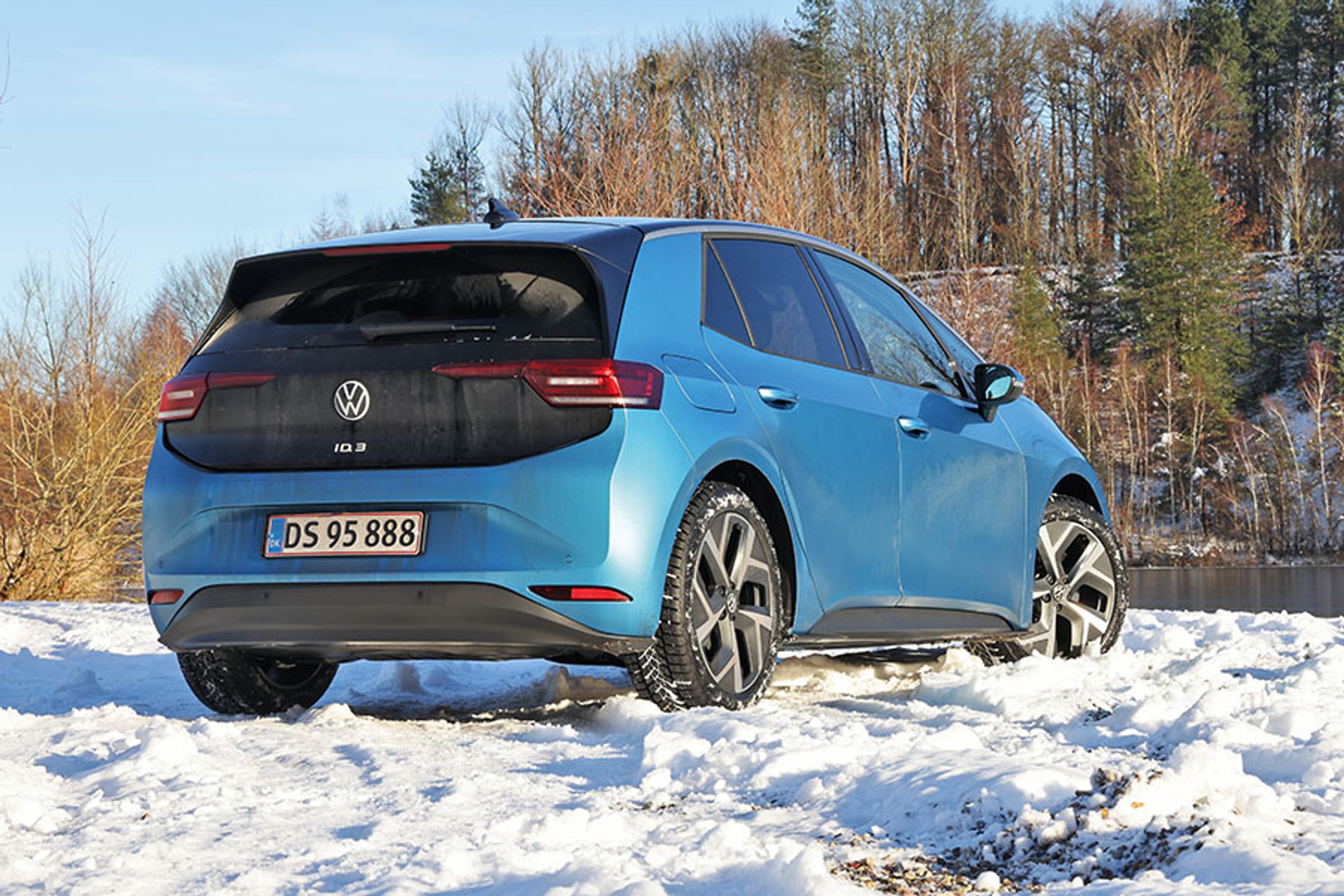 En blå VW ID.3 set bagfra holder i sne med en skovsø i baggrunden