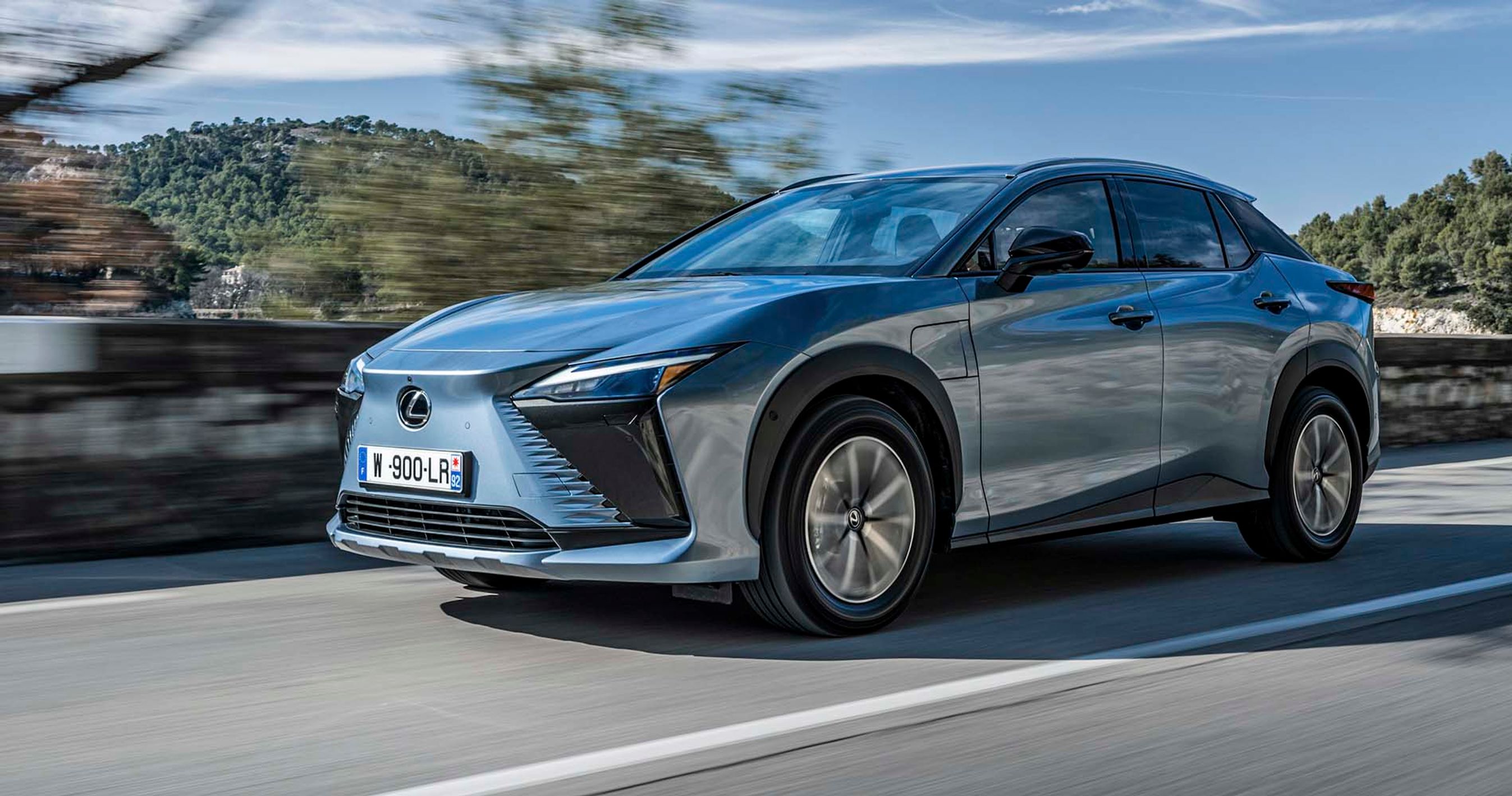 En Lexus RZ kører på bjergvej med udsigt til havet i baggrunden