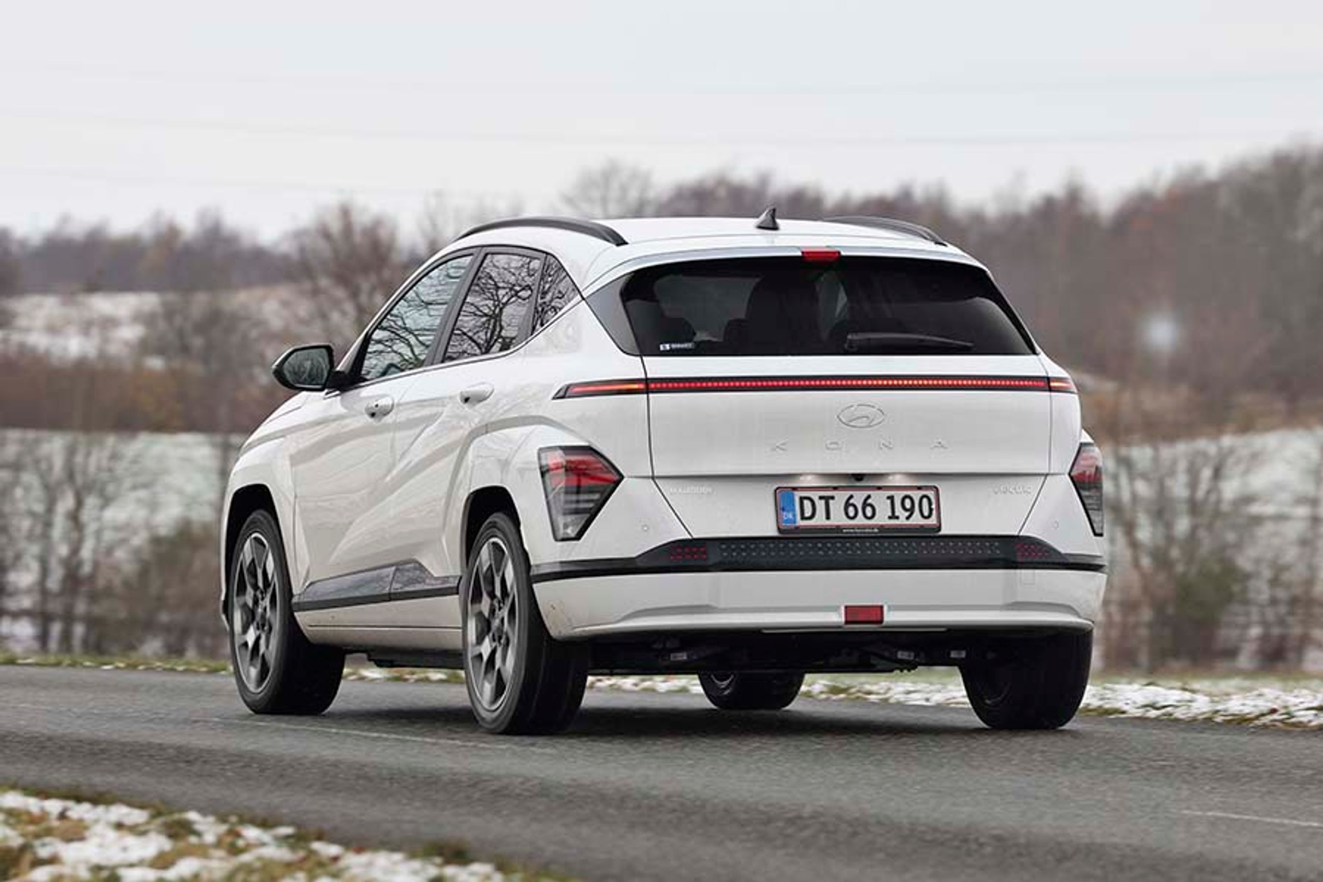 En hvid Hyundai Kona Electric set bagfra, mens den kører i snelandskab
